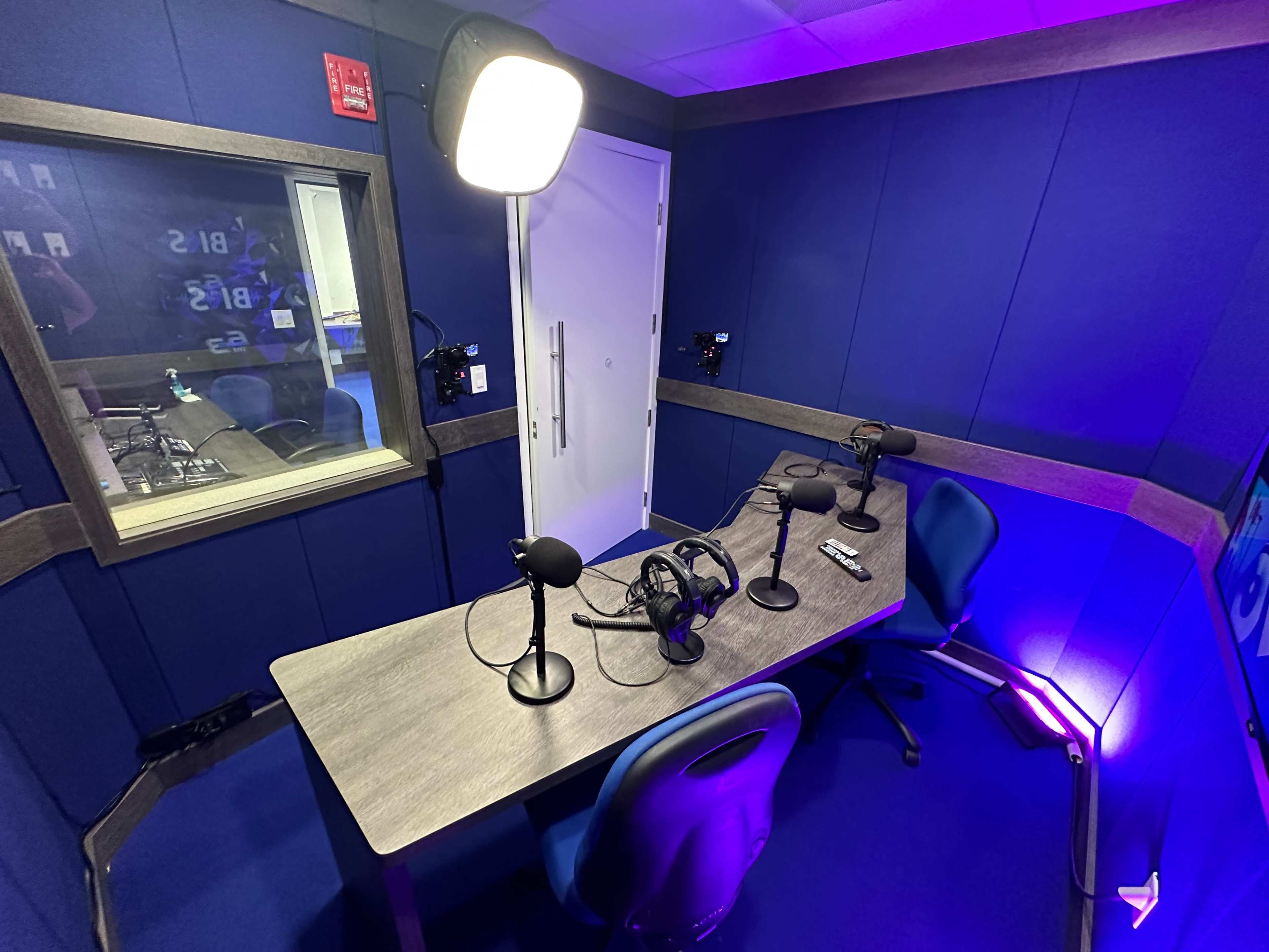A soundproof recording studio with a table set for four microphones and headphones, featuring blue walls and adjustable lighting.