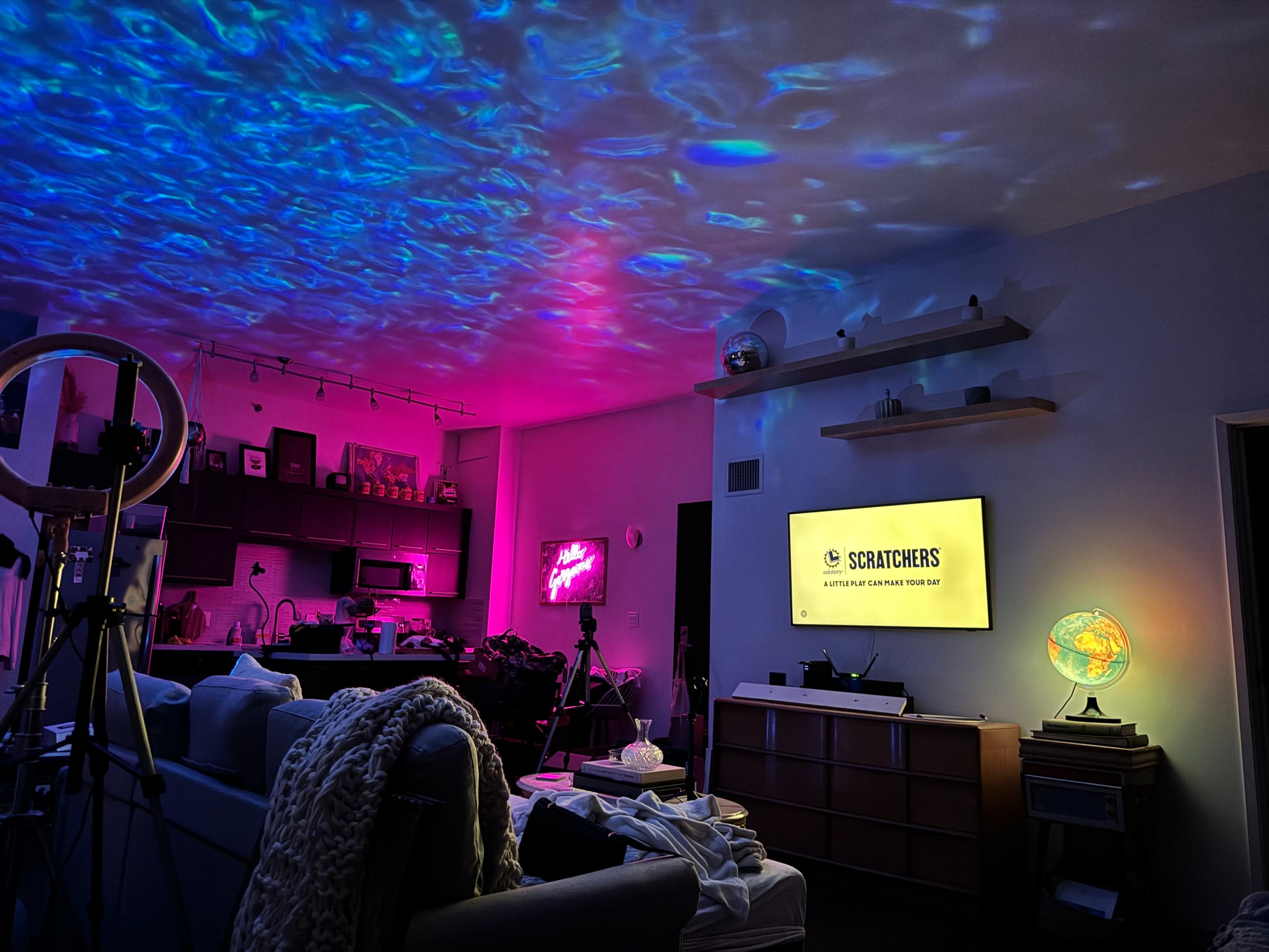 A living room is illuminated with colorful light projections on the ceiling, featuring a television displaying text and various decorative elements throughout the space.