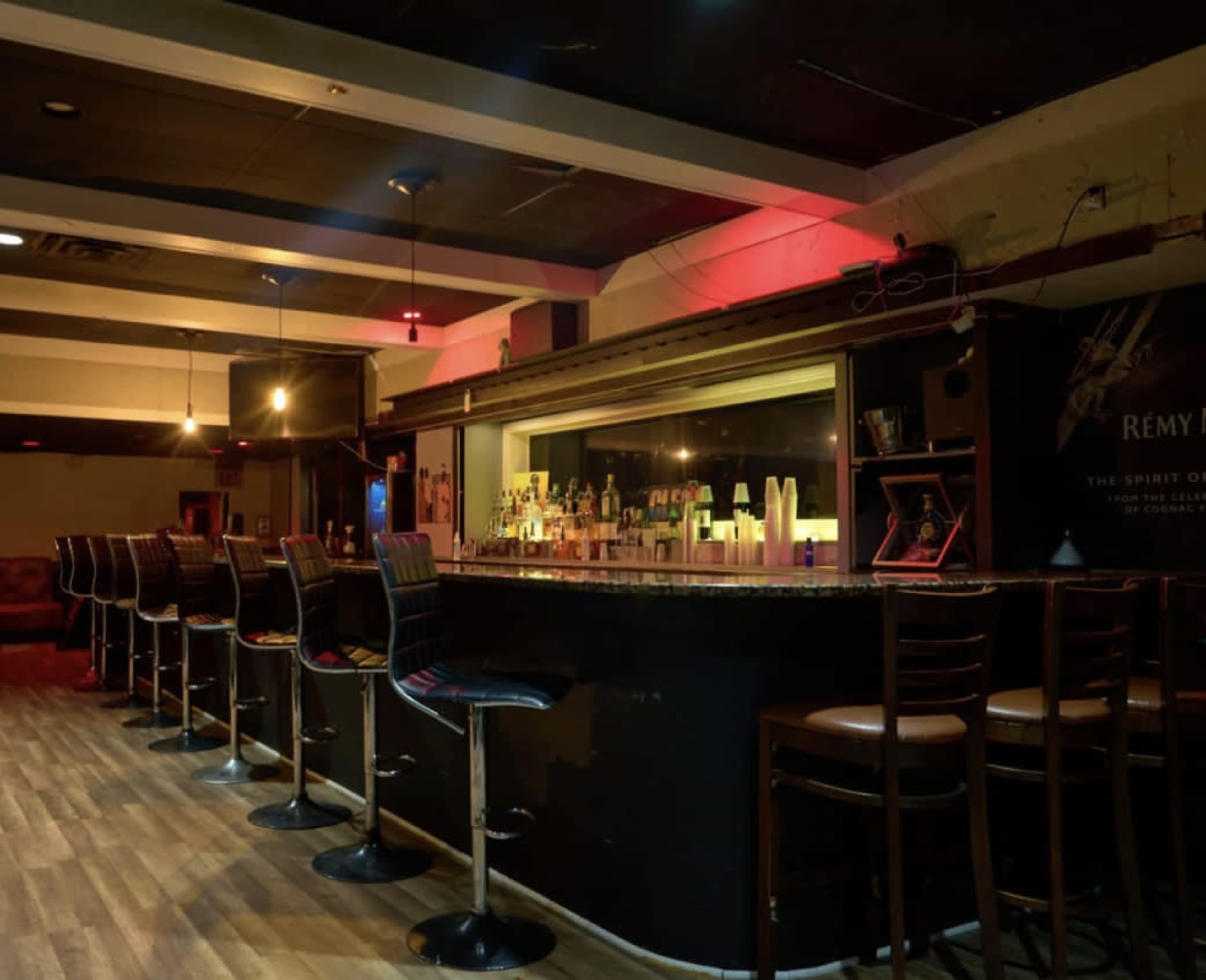 An empty bar with several high-backed chairs arranged along a dark countertop, illuminated by soft lighting.
