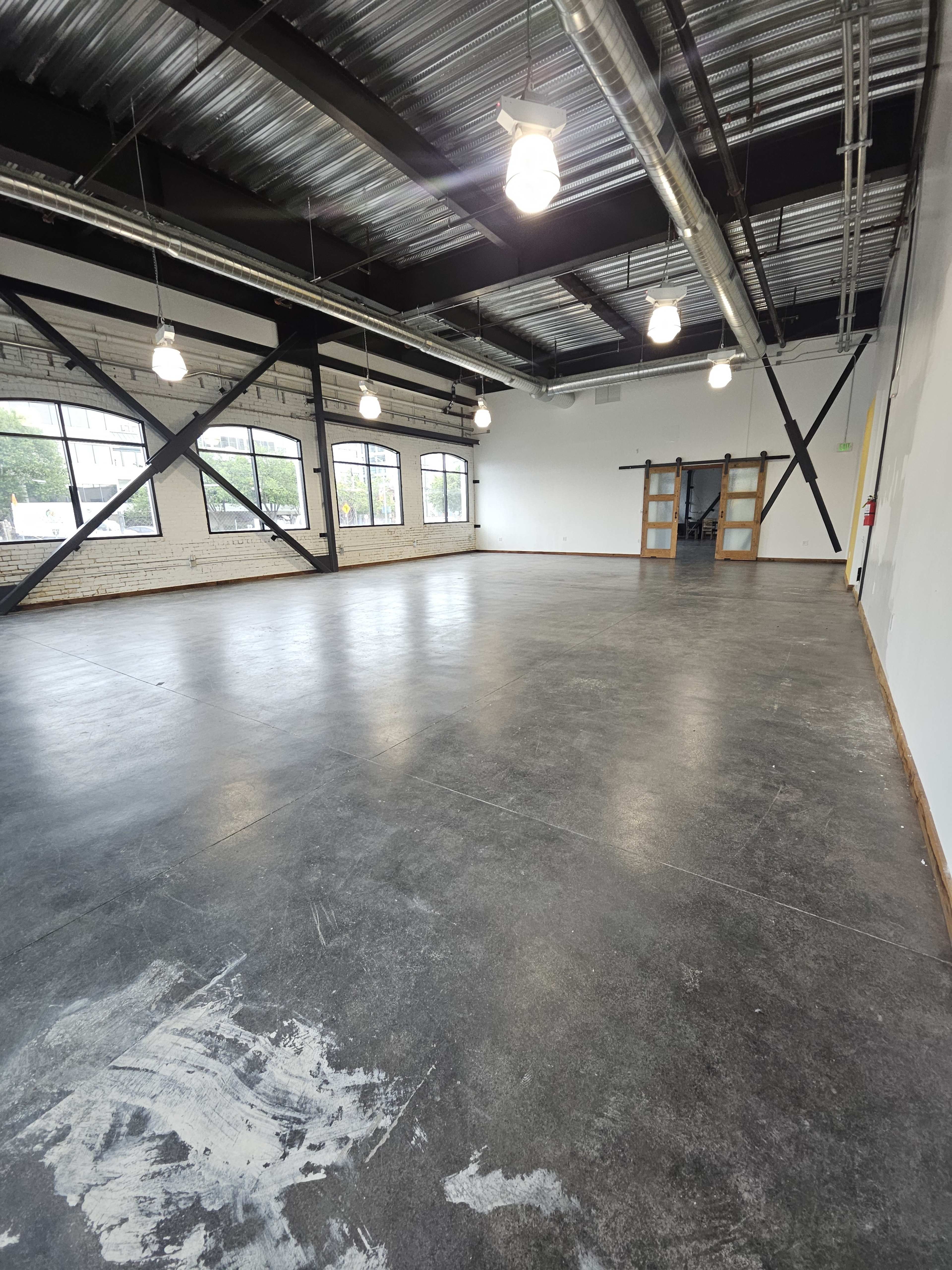 A spacious industrial-style room with polished concrete flooring and large windows along the sidewalls.