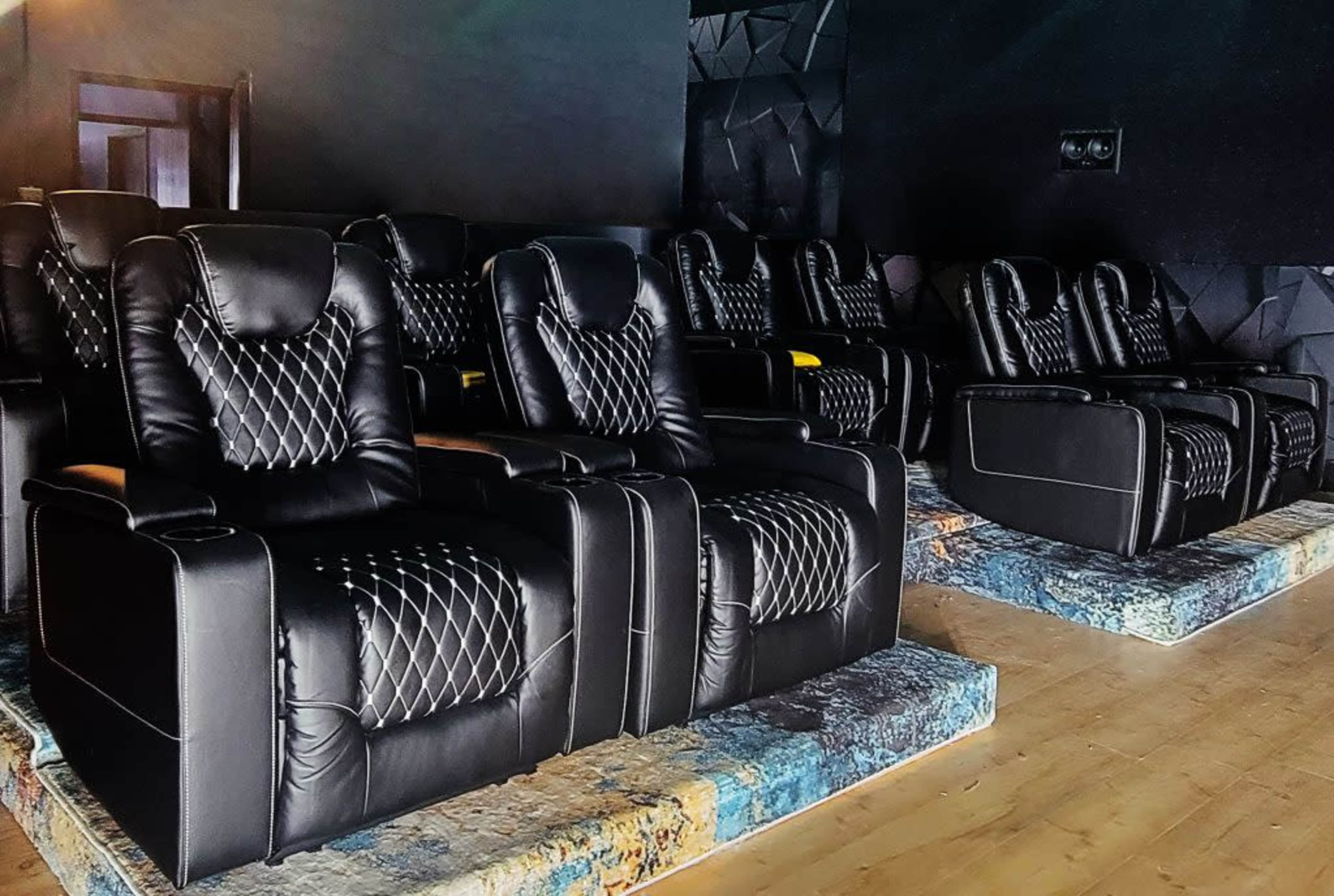 The image shows a row of luxury black recliner chairs arranged in a darkened theater setting.