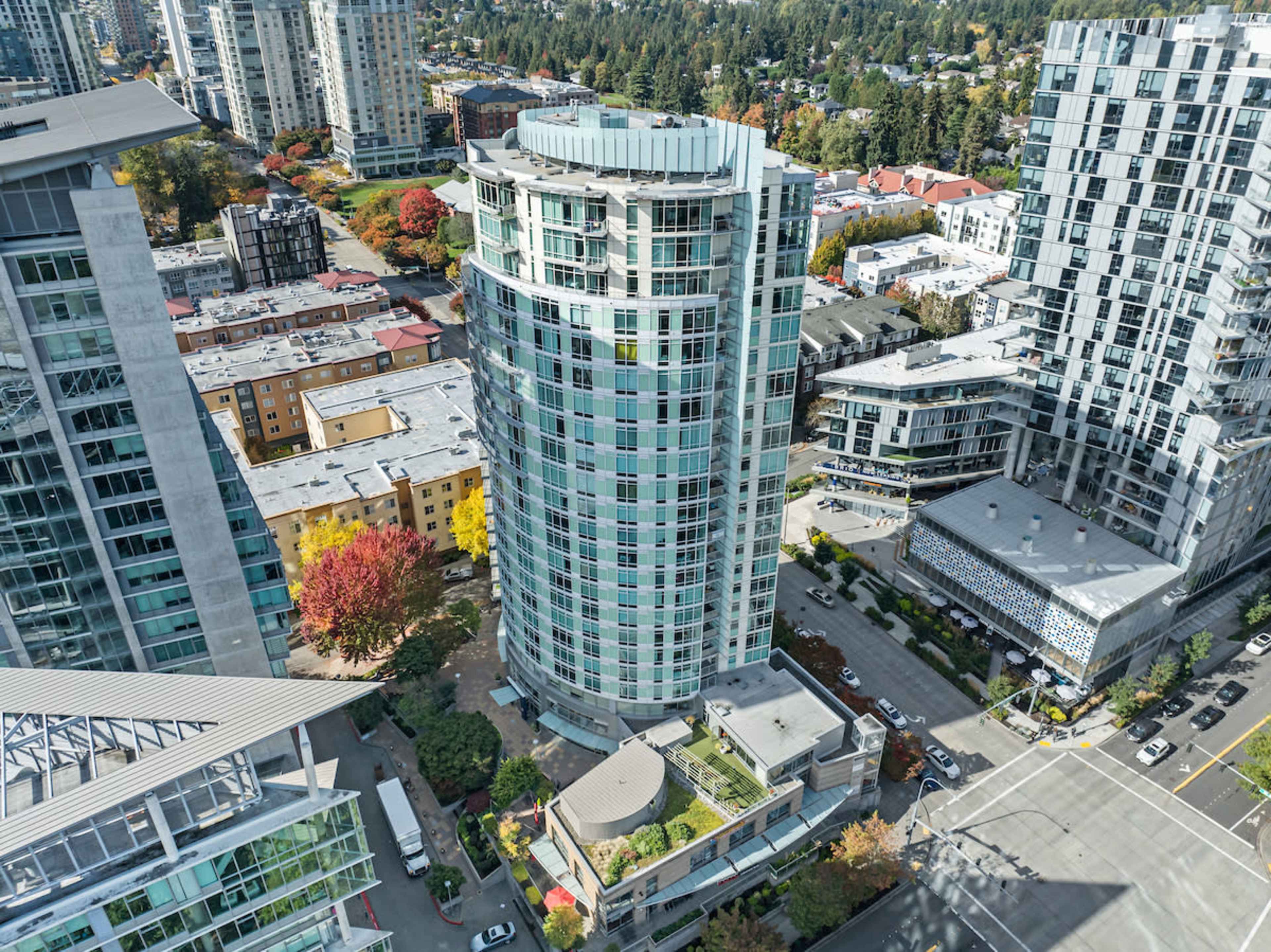 Aerial view of a modern residential high-rise building surrounded by other buildings and green trees in an urban setting.