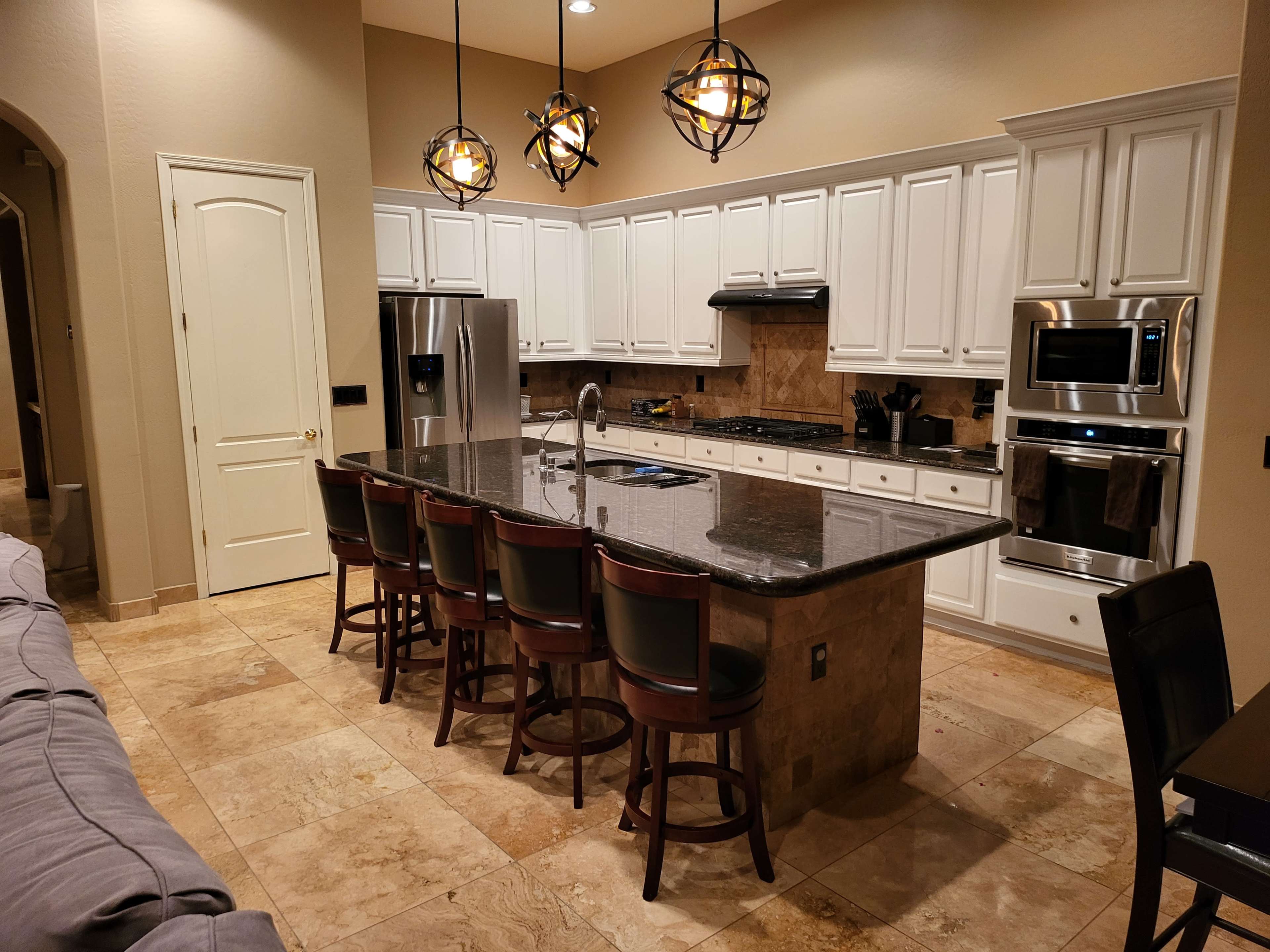 The image shows a modern kitchen with white cabinetry, a large granite island with seating for eight, and stainless steel appliances.