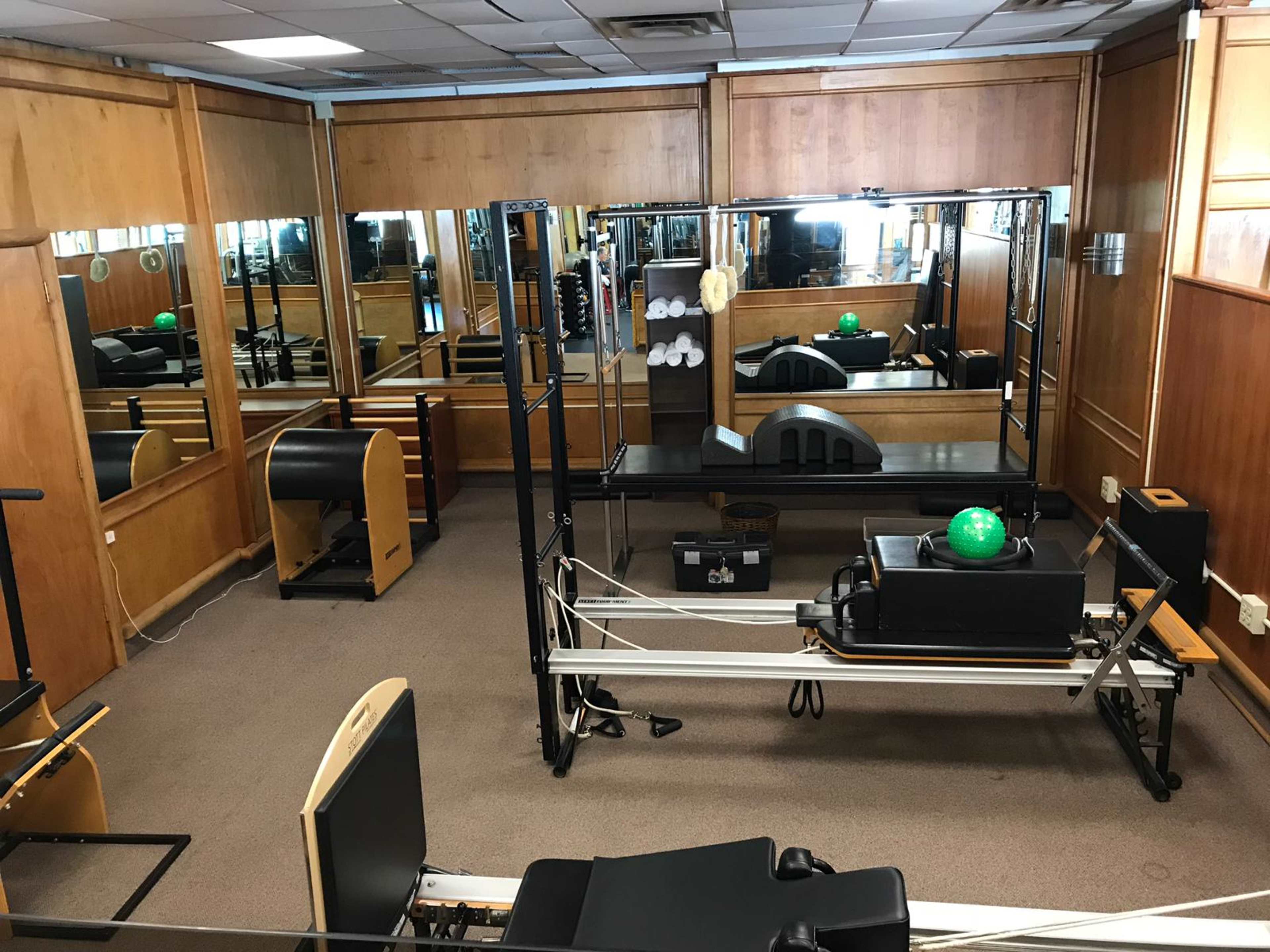 A Pilates studio with wooden walls, mirrors, and various exercise equipment arranged around the room.