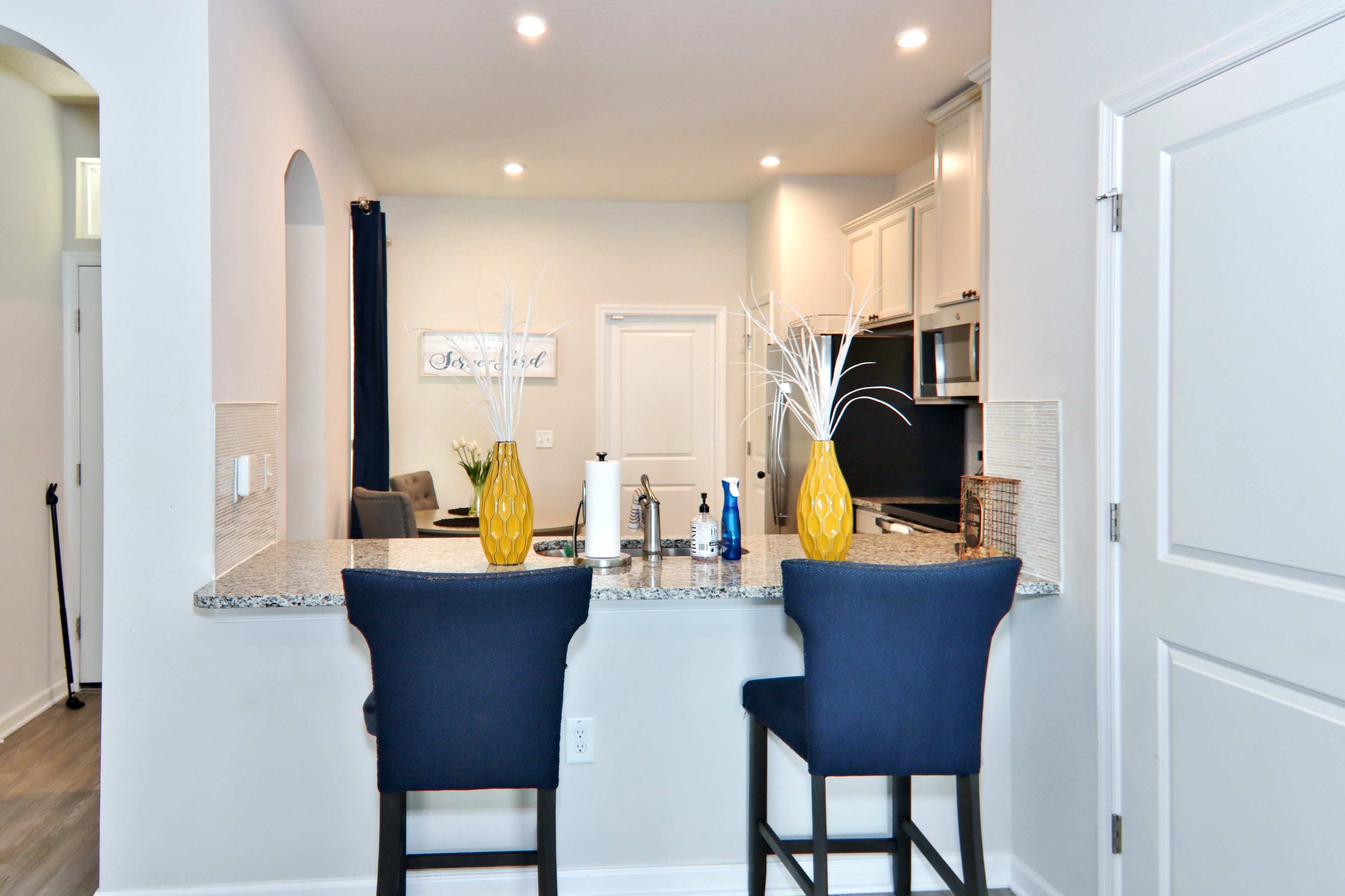 A modern kitchen with a granite countertop, two blue barstools, and decorative vases on the surface.