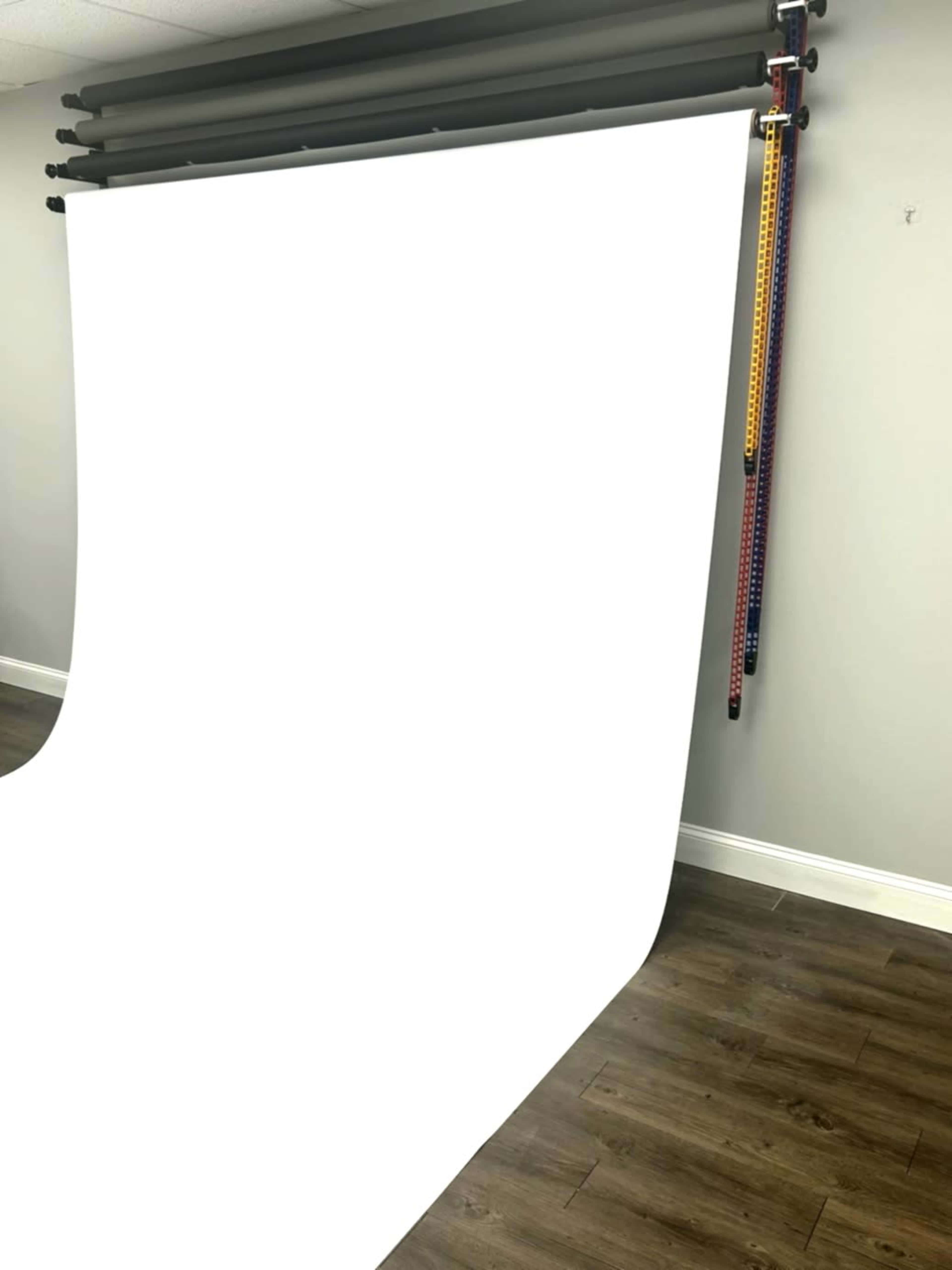 A white backdrop is hung from a rack against a wall in a room with wooden flooring.