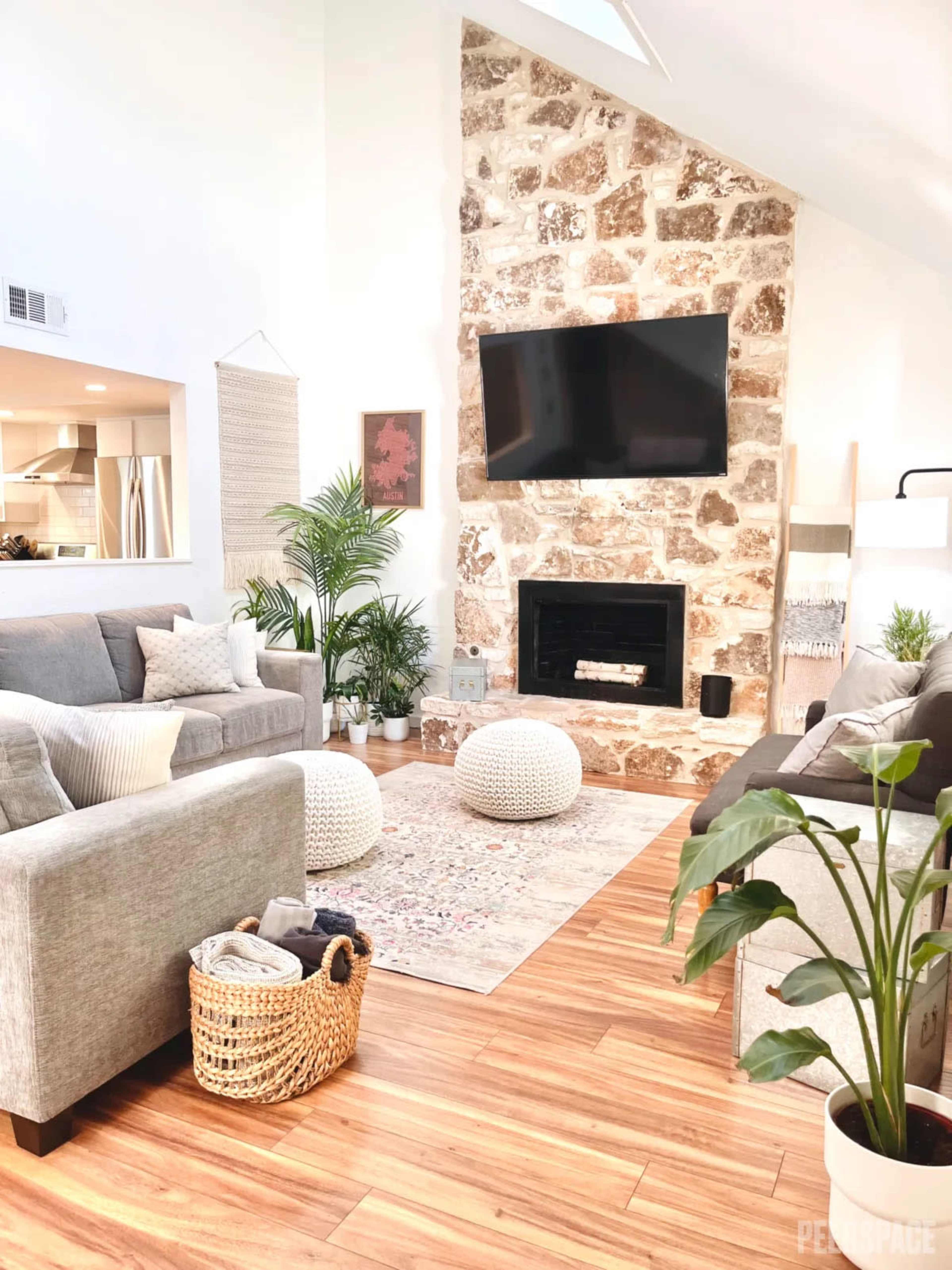 The living room features a stone accent wall with a mounted television, a central fireplace, and modern furniture arranged around a patterned rug.