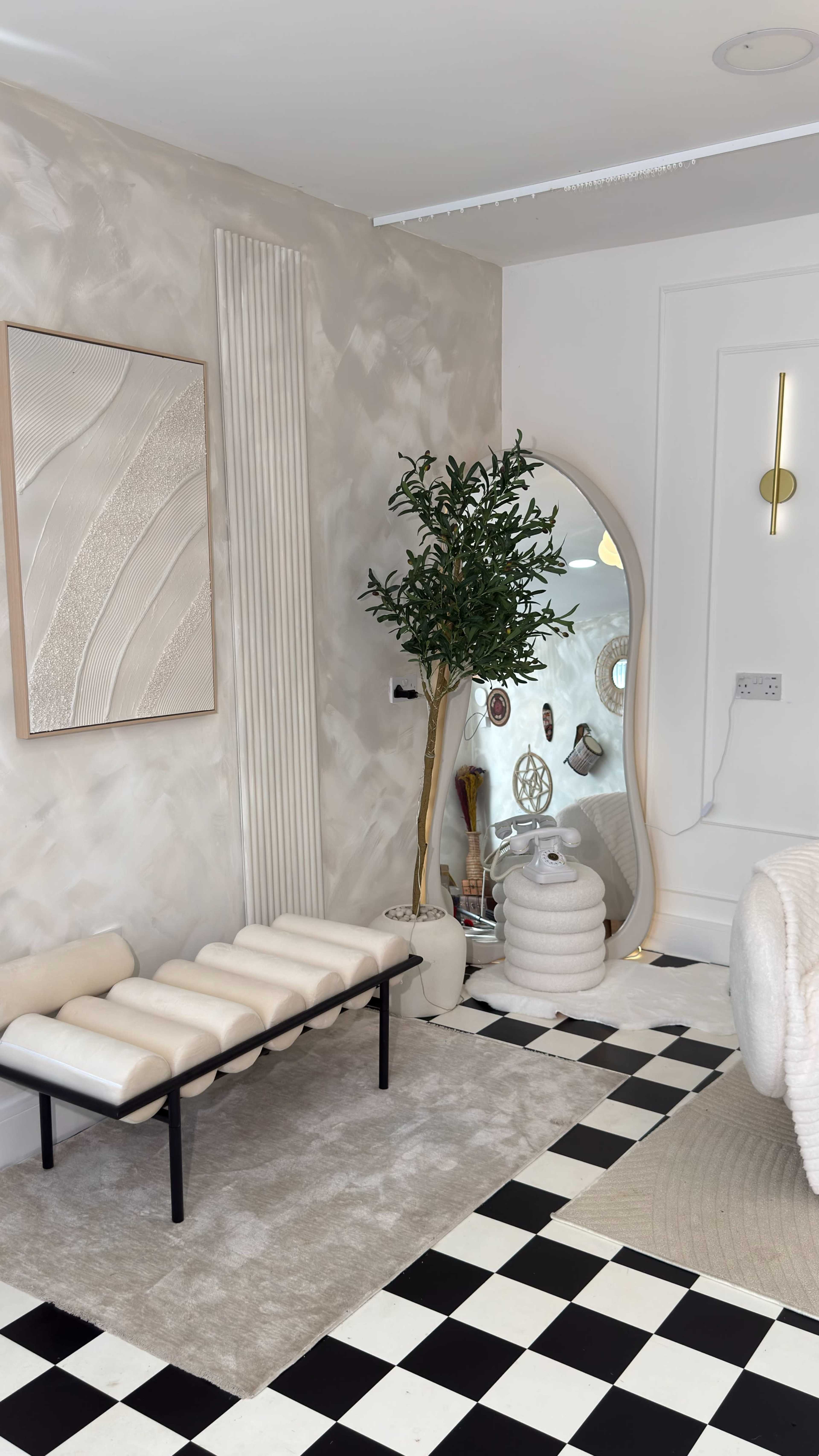 The image shows a modern interior space featuring a bench, a decorative plant, a large mirror, and a checkered floor.