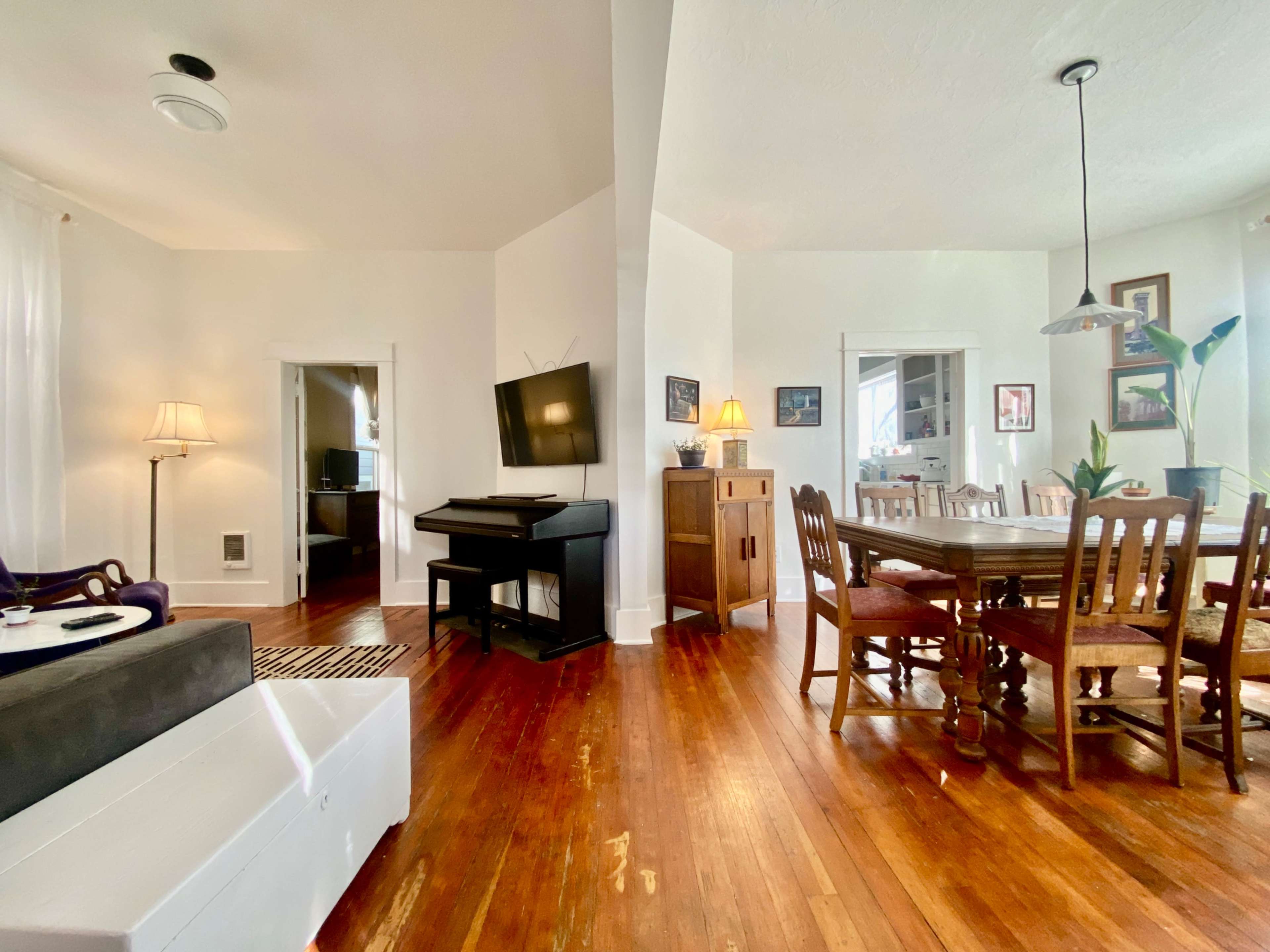A cozy living and dining area with wooden flooring, a sitting space featuring a couch and a TV, and a dining table surrounded by chairs.