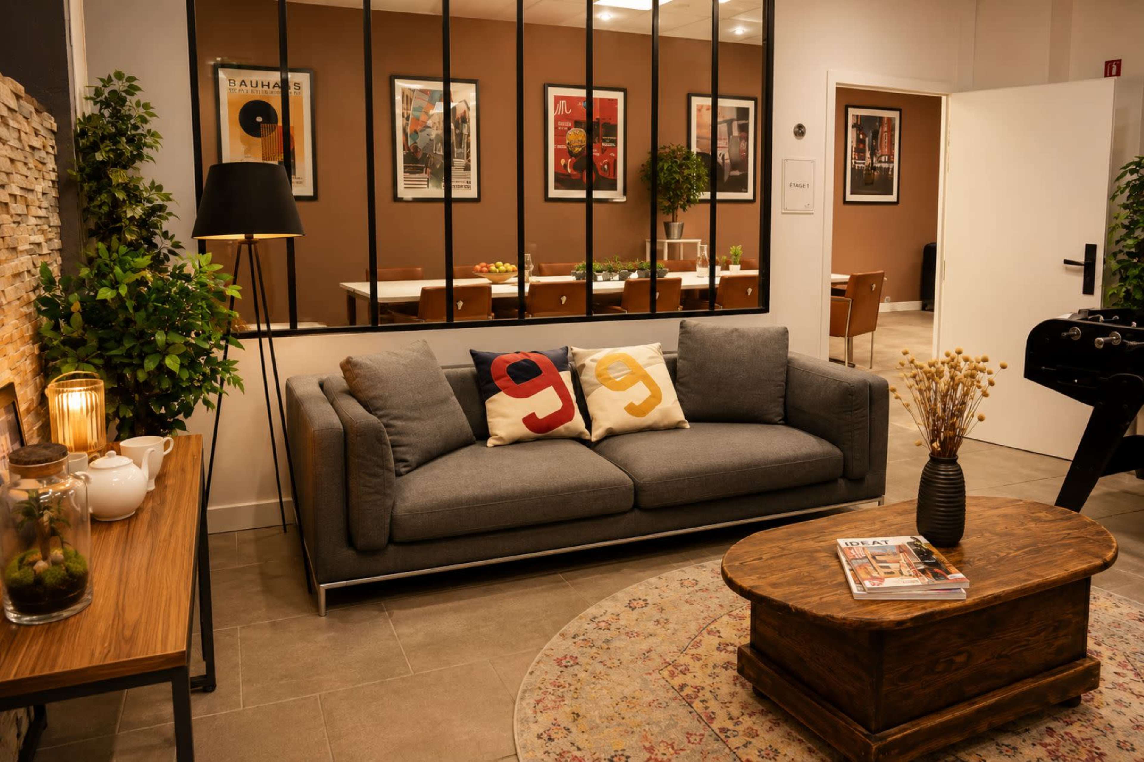 The image shows a modern living room with a gray sofa, decorative throw pillows, a wooden coffee table, and a mirrored wall reflecting framed artwork.