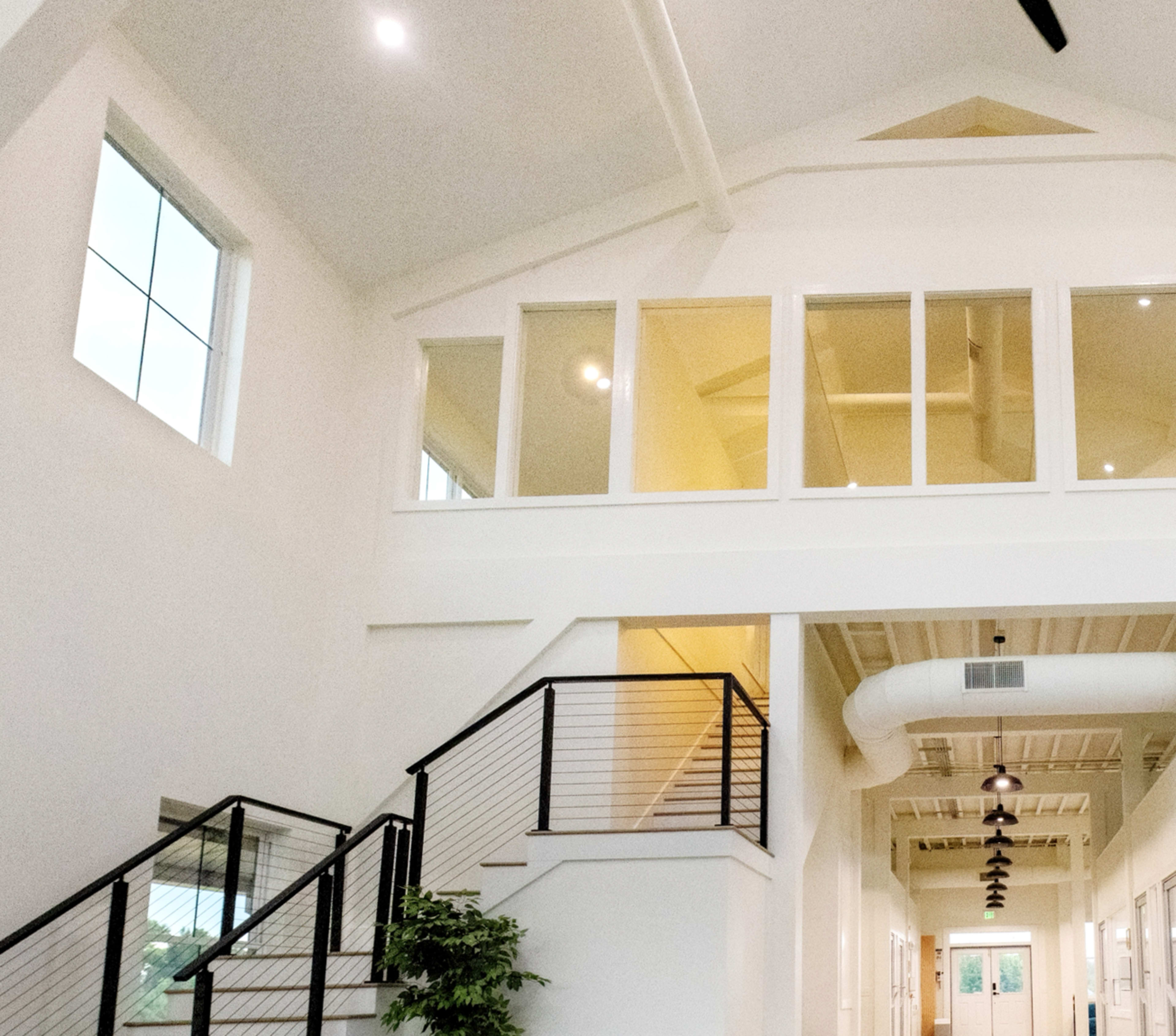 The image shows a modern, open-concept interior with a staircase, large windows, and pendant lighting.