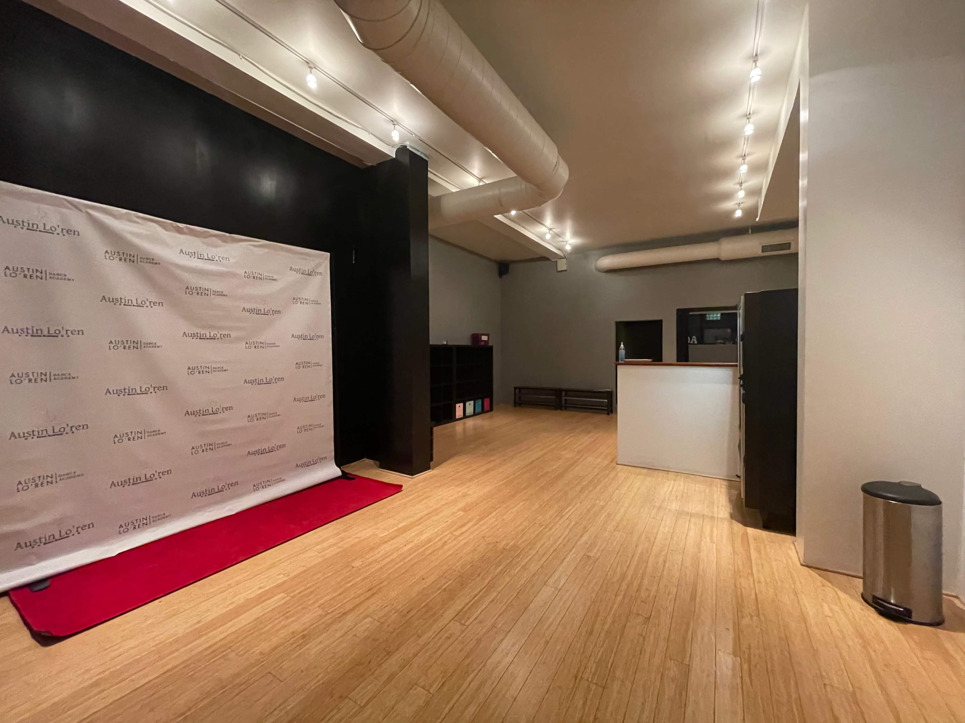 The image shows an empty room with a red carpet in front of a branded backdrop and a reception area on the right.