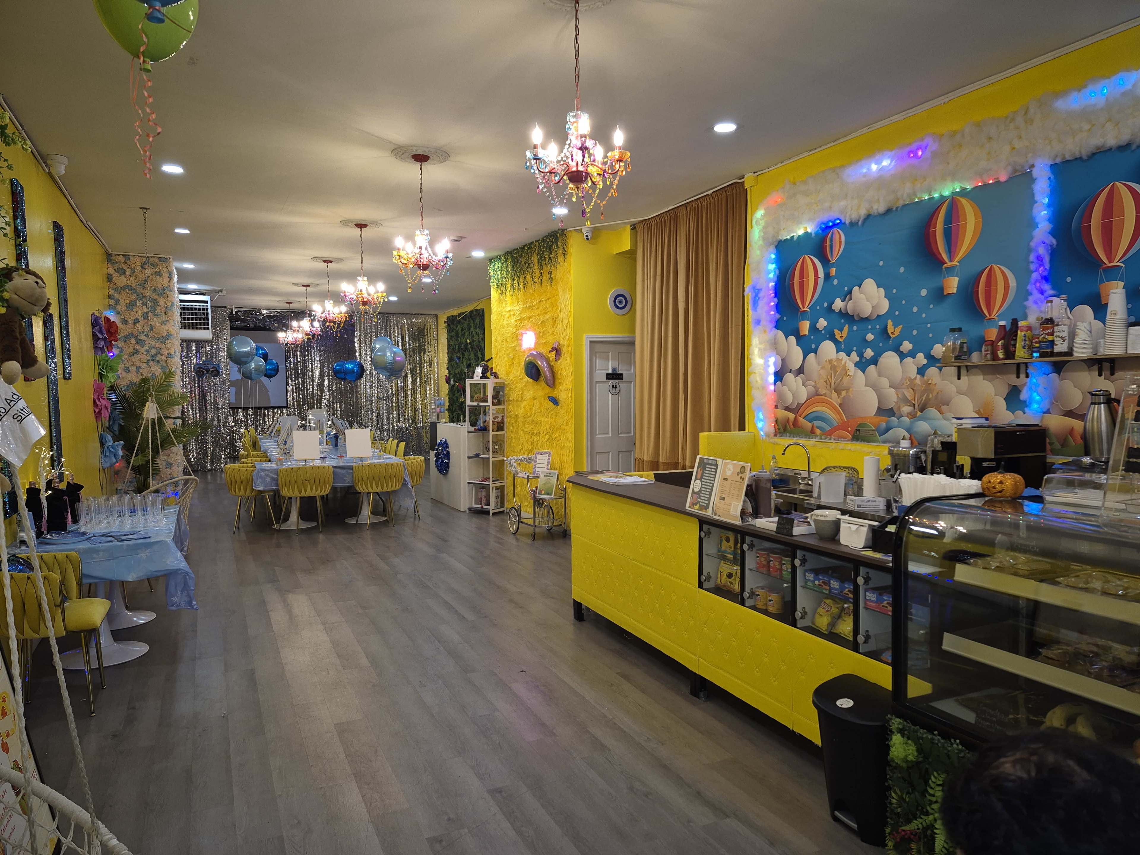 The image shows a brightly decorated café featuring yellow walls, colorful murals, and a variety of seating arrangements.