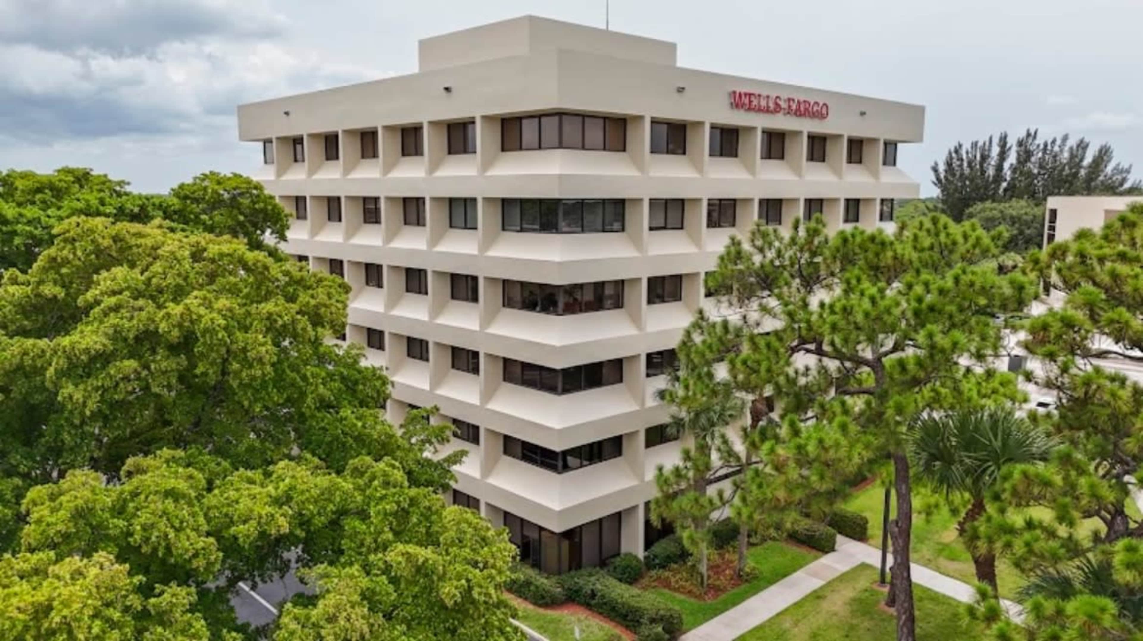 The image shows a multi-story Wells Fargo office building surrounded by greenery and trees.