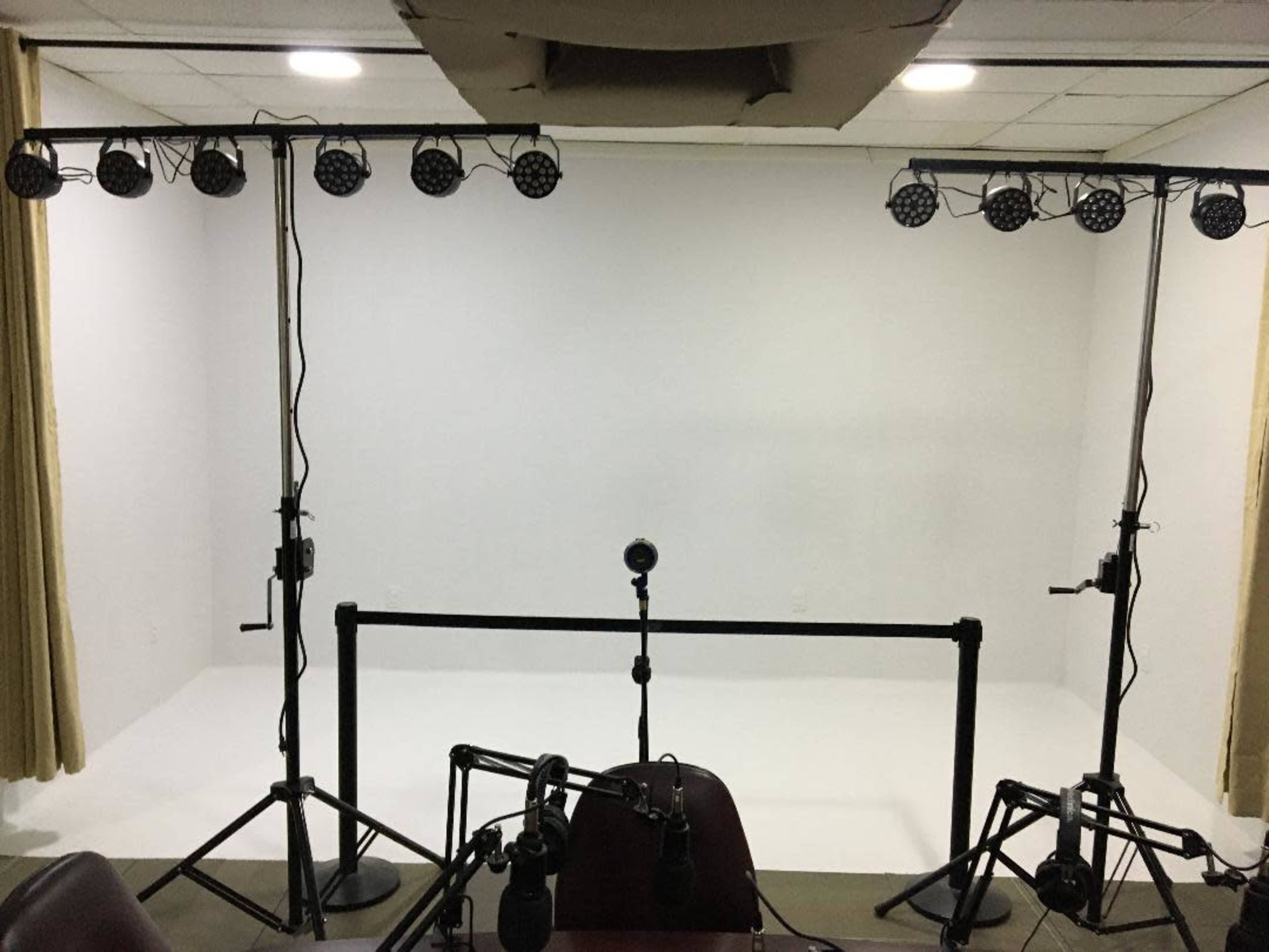 The image shows a bare studio space with a white backdrop, lighting stands equipped with multiple lights, and a microphone setup on a table.