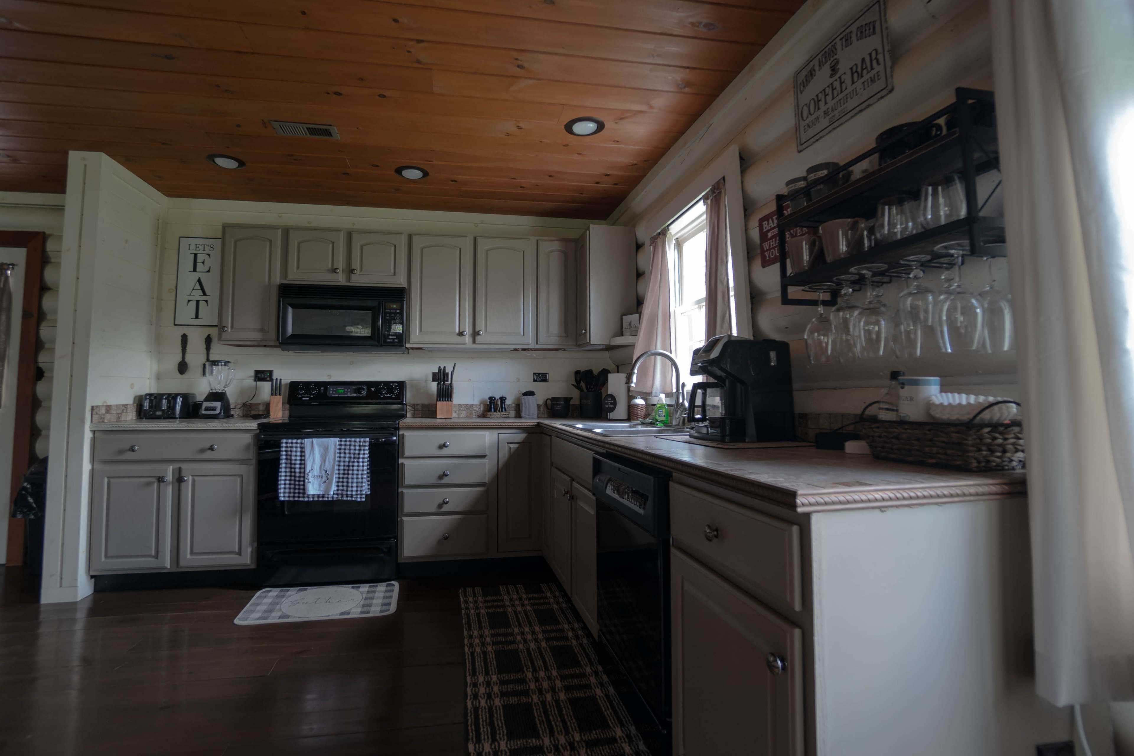 The image shows a kitchen with wooden ceiling panels, light-colored cabinets, and stainless steel appliances, including a microwave and coffee maker.