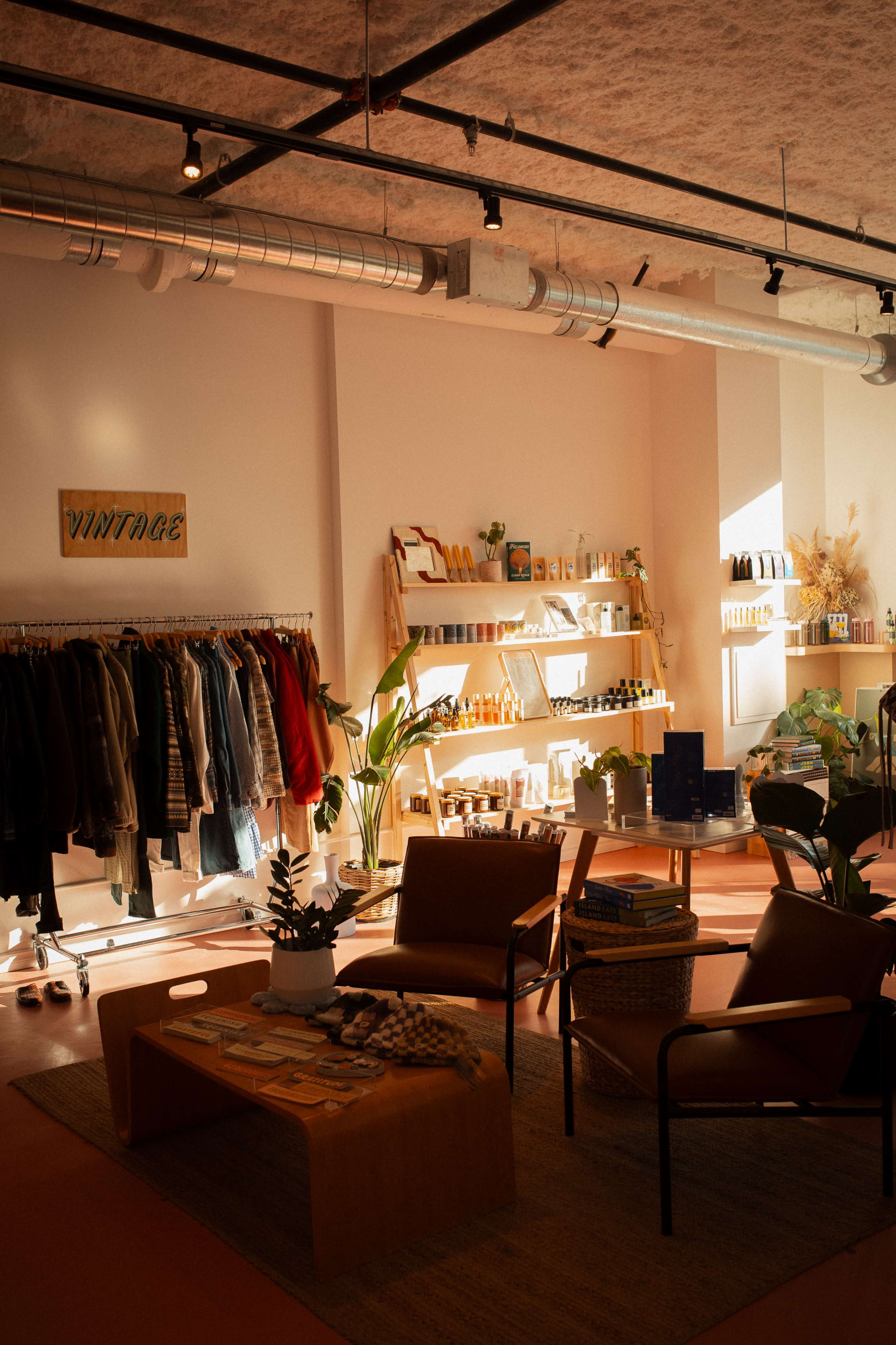 A vintage-style shop interior featuring clothing racks, shelves lined with products, and seating areas with plants and decor.