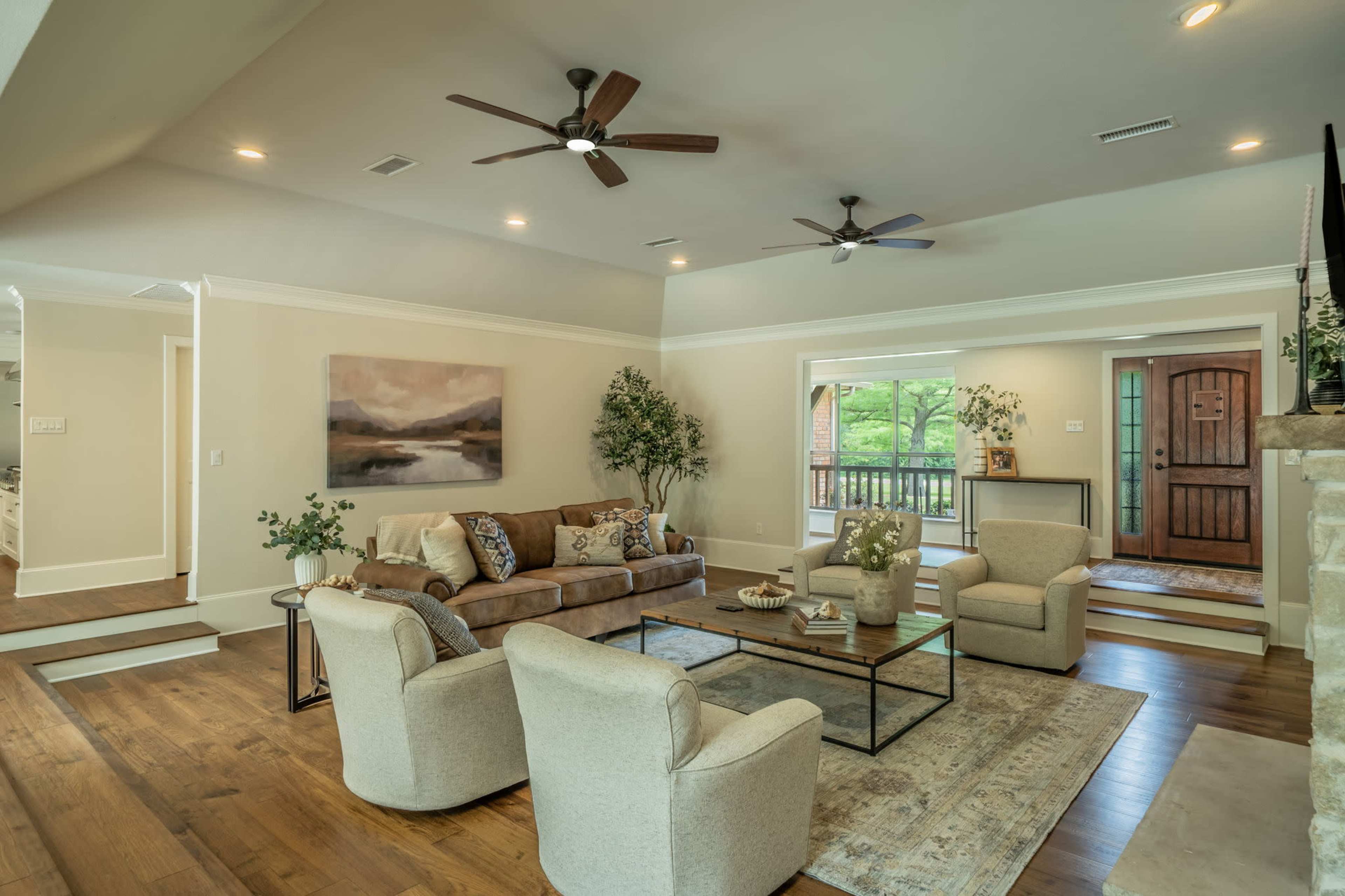The living room features a comfortable seating arrangement with a sofa and chairs, a coffee table, and large windows offering views of the outdoors.