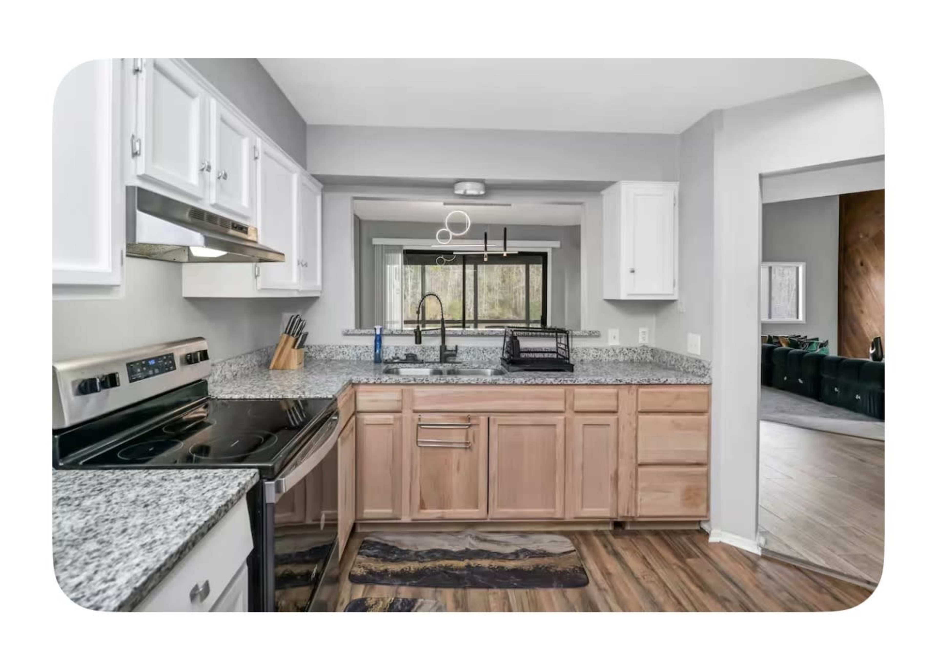 The image shows a modern kitchen with granite countertops, white cabinets, and stainless steel appliances, leading to a view of a living area.