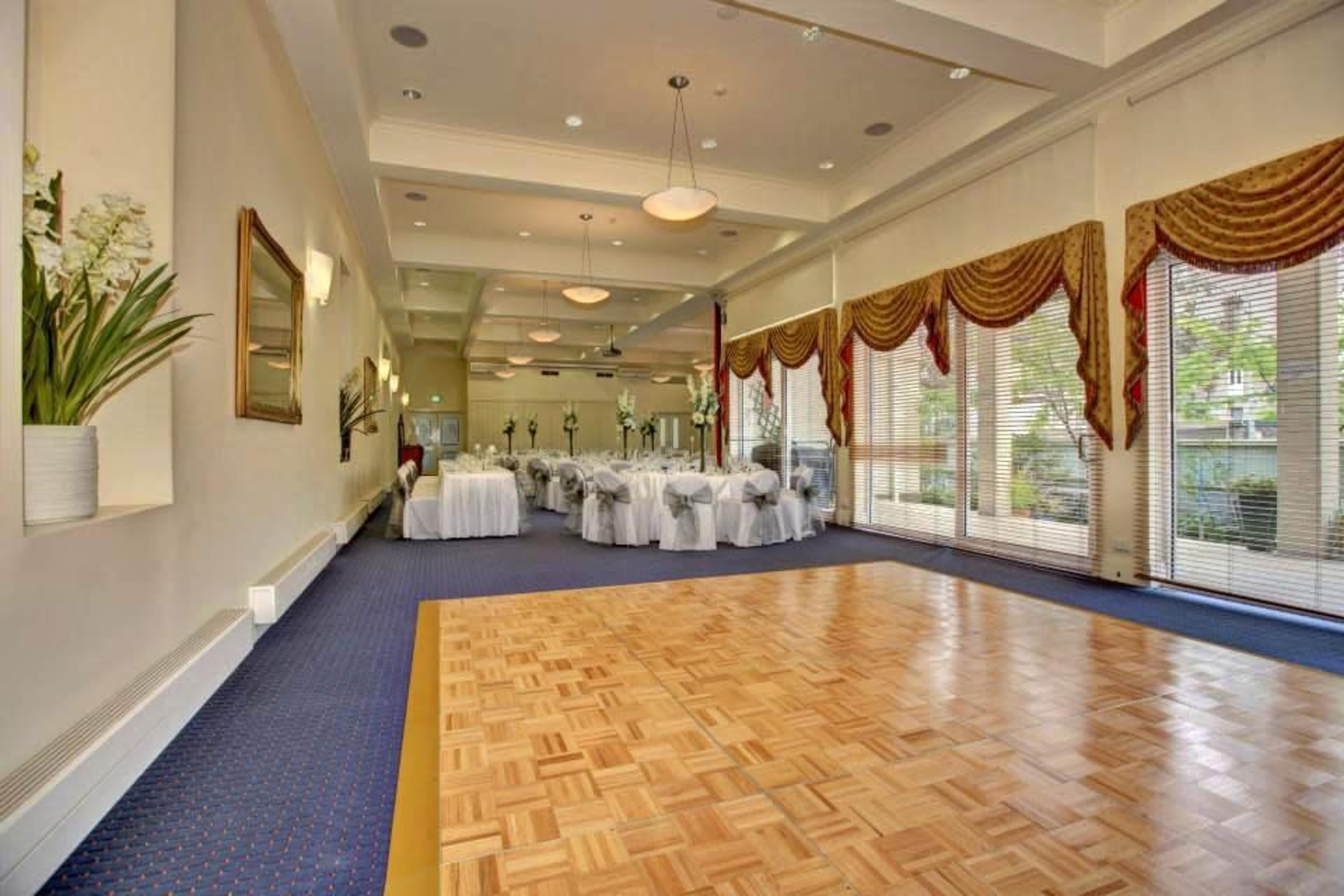 A spacious banquet hall features a wooden dance floor and rows of elegantly set tables with white linens.