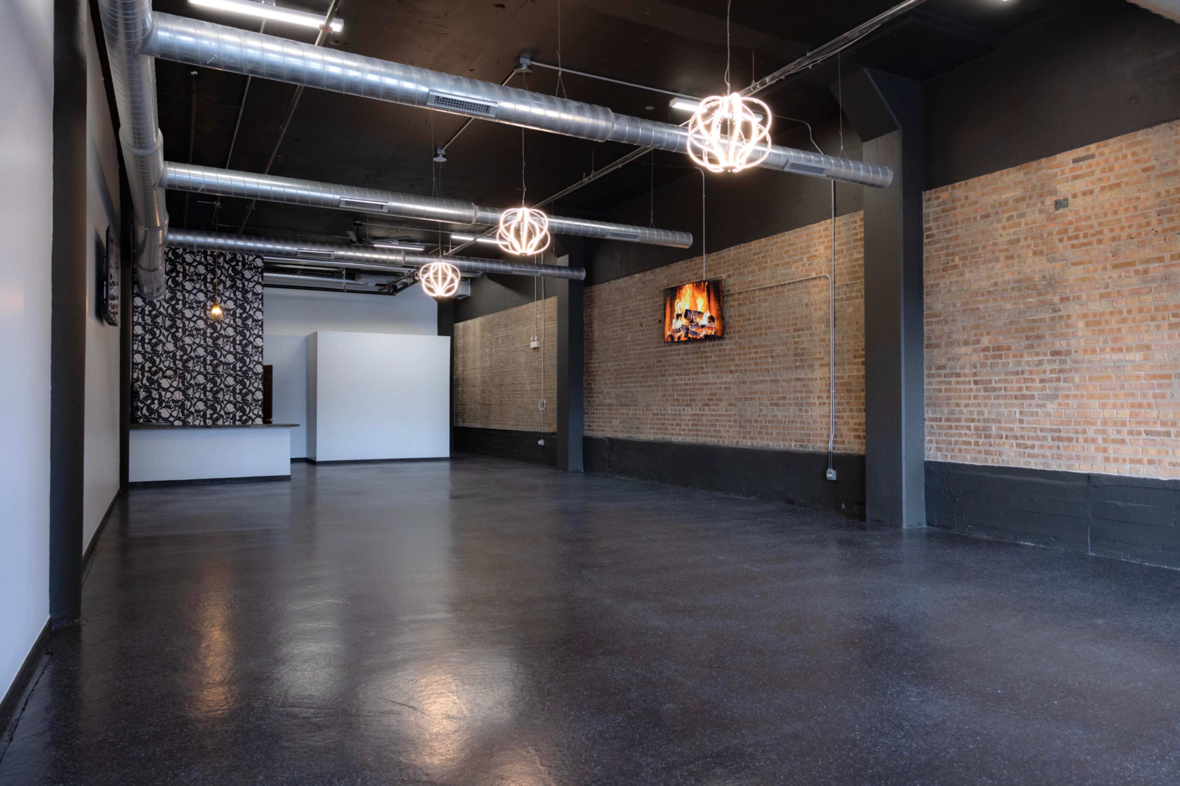 The image shows a spacious, empty interior with exposed brick walls, industrial light fixtures, and polished black flooring.