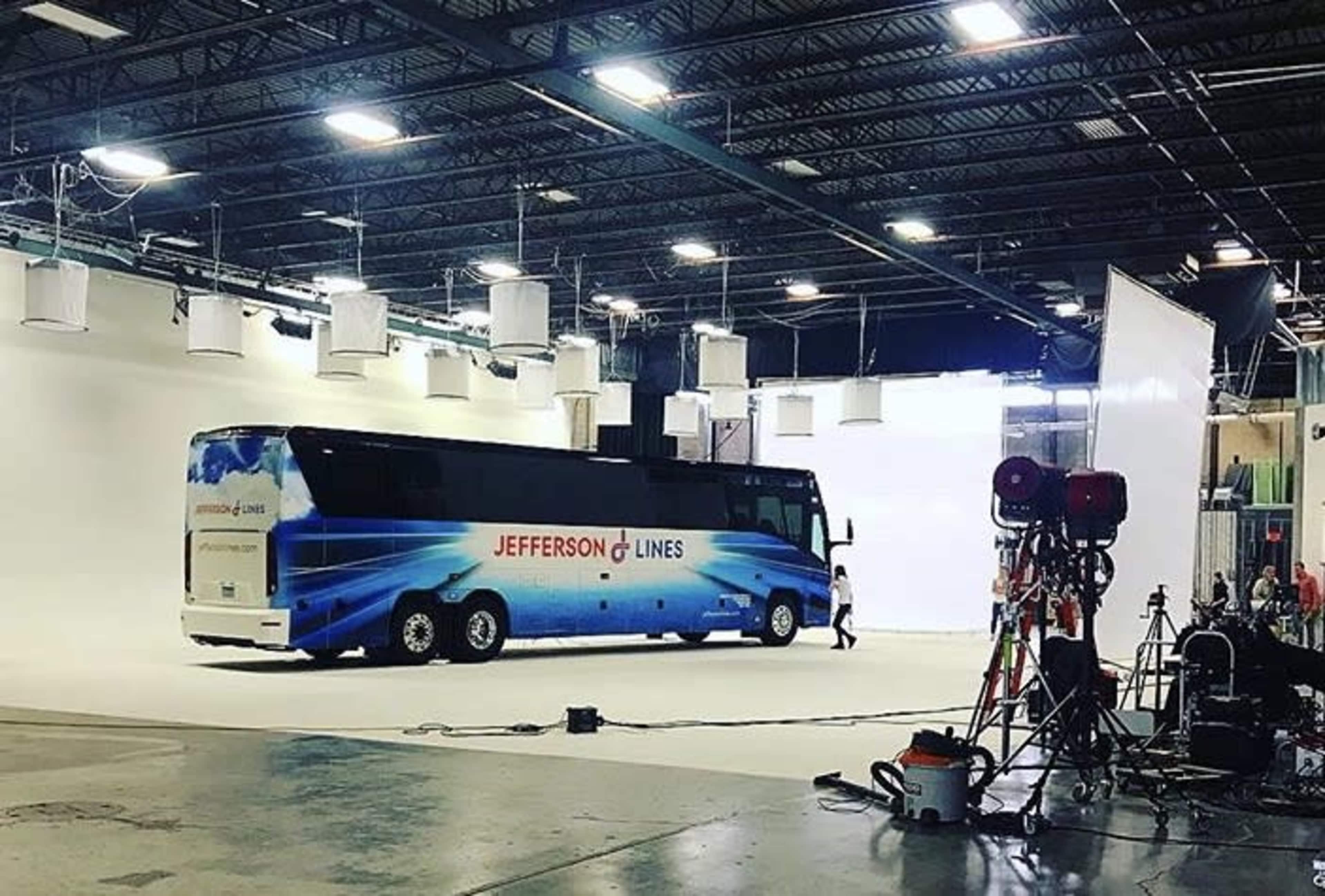 A large tour bus labeled "Jefferson Lines" is positioned in a well-lit studio space, surrounded by film equipment and a white backdrop.