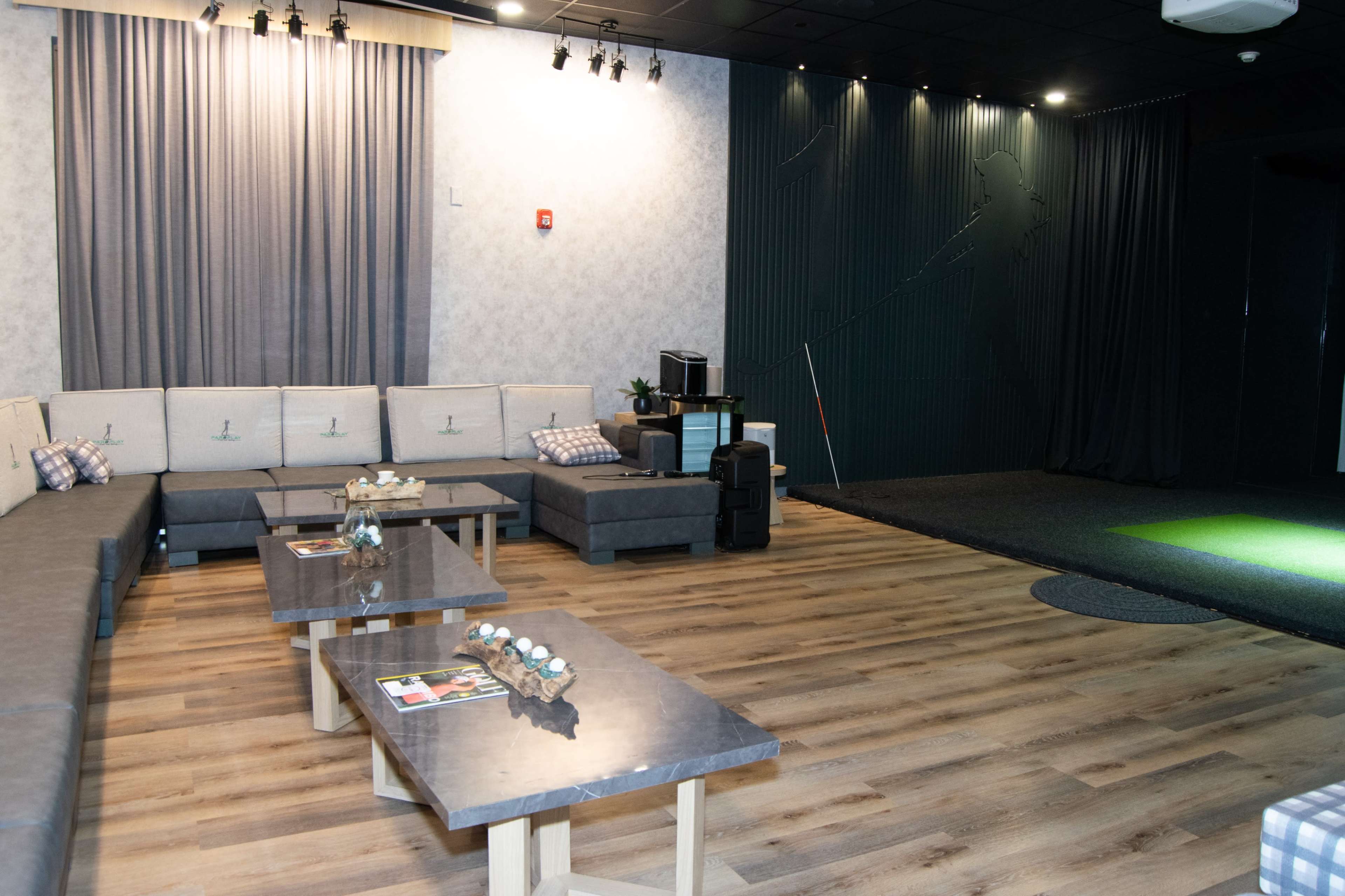 A modern lounge area with a sectional sofa, low tables, and a space with a putting green in the corner.