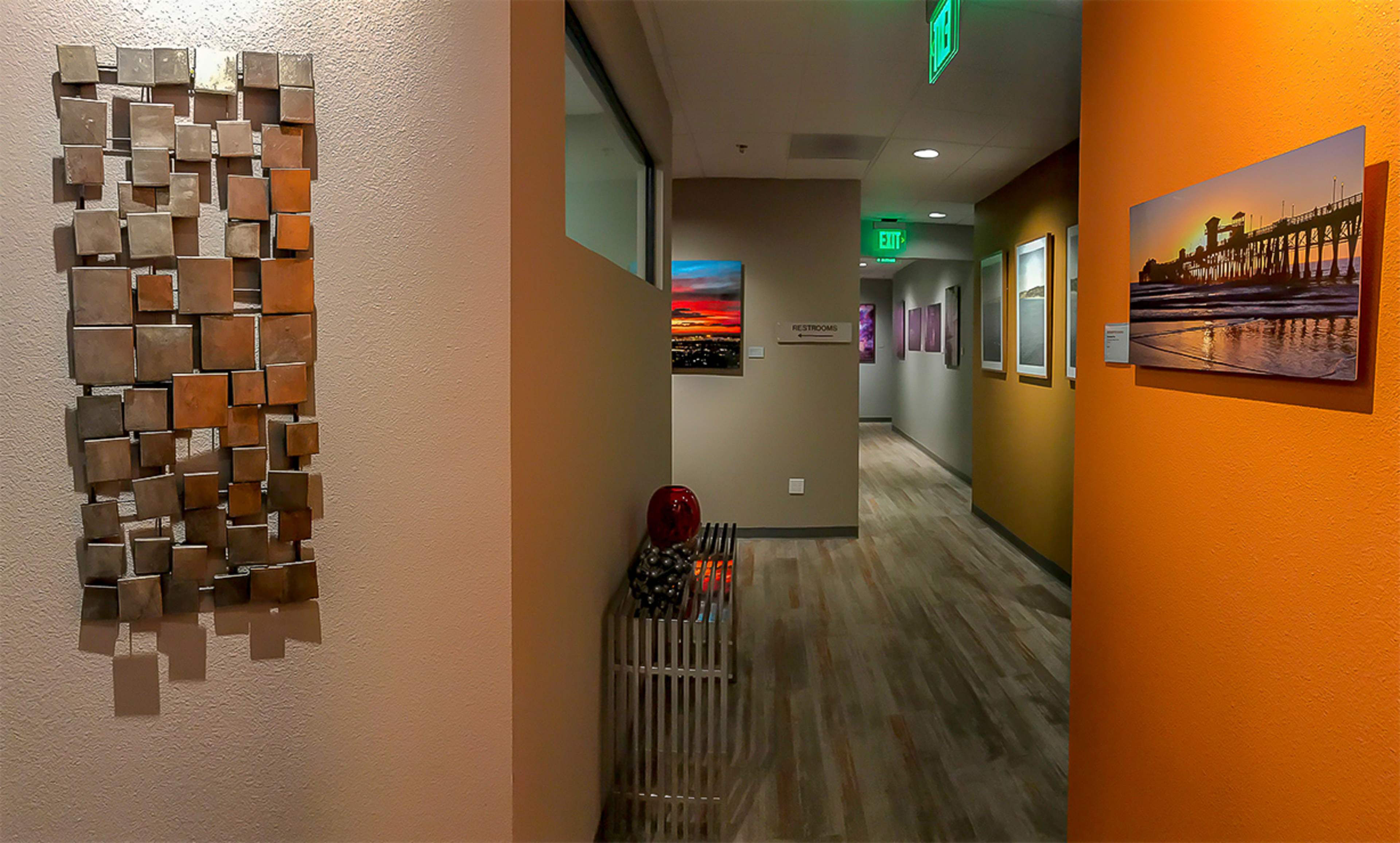 A hallway features a metallic wall art piece on one side, with framed photographs lining the walls and warm lighting illuminating the space.