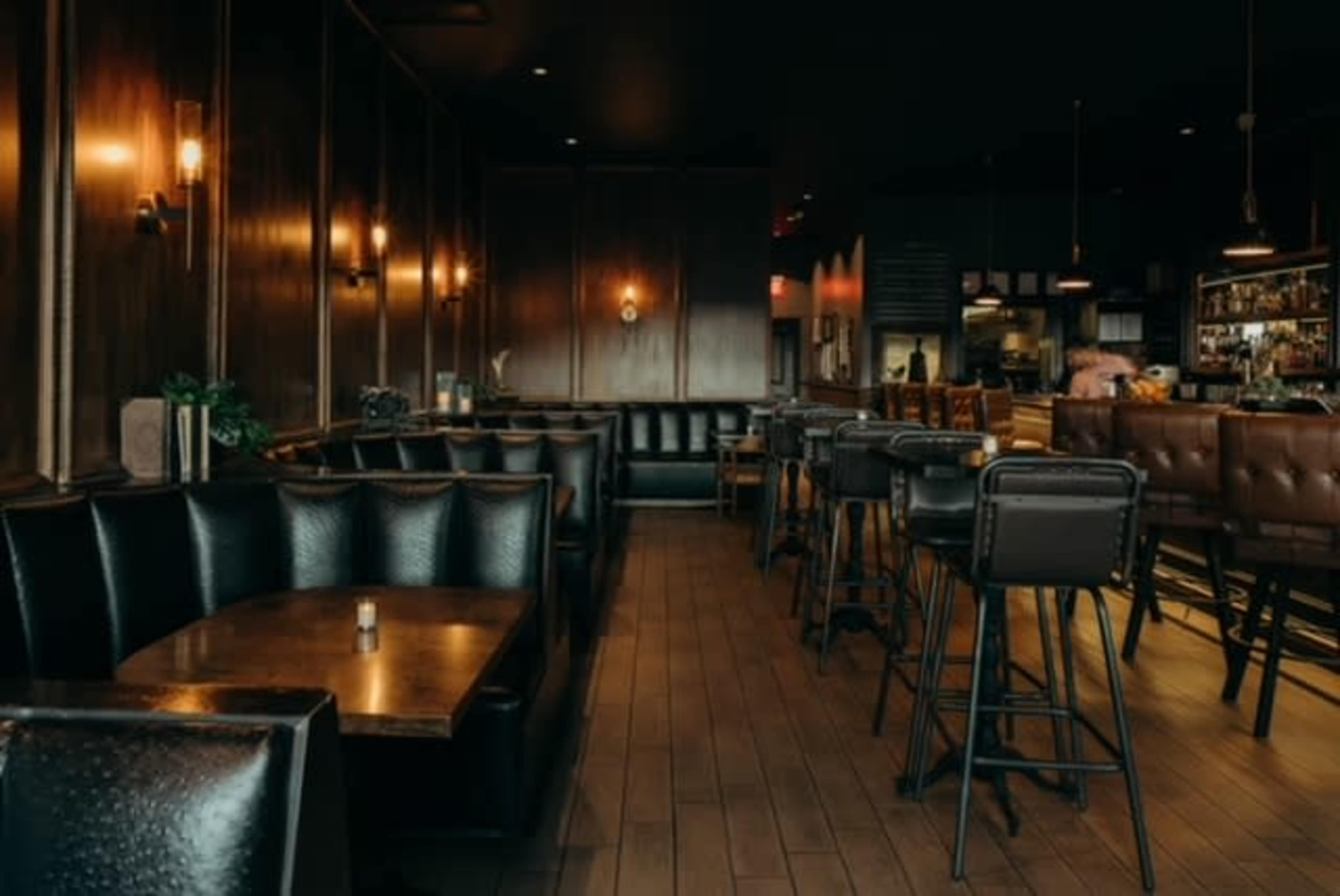 The image shows a dimly lit restaurant interior with dark wooden walls, leather seating, and a bar area in the background.