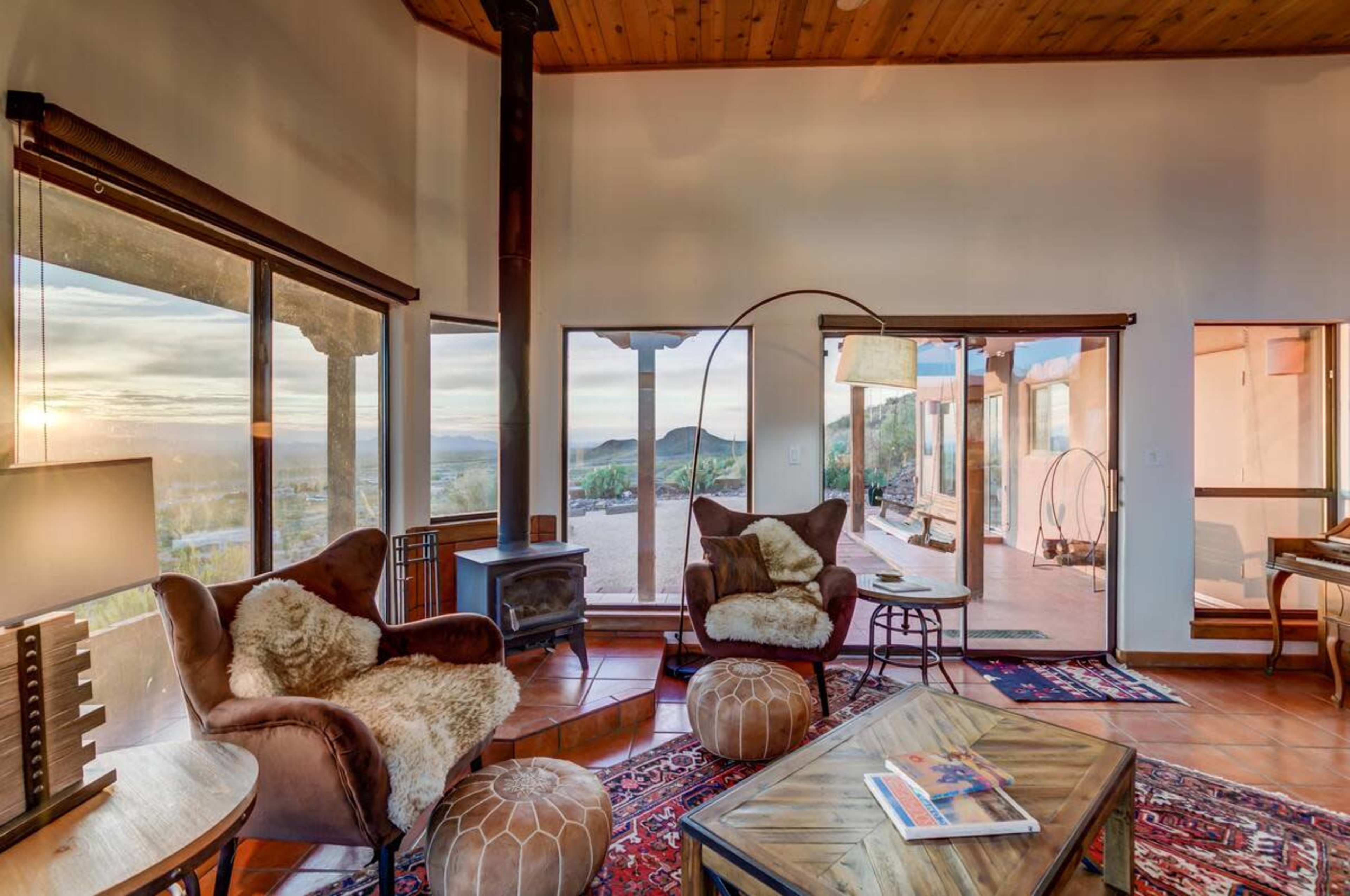 The image shows a cozy living room featuring two armchairs, a wooden coffee table, and large windows that provide a view of the outdoors.