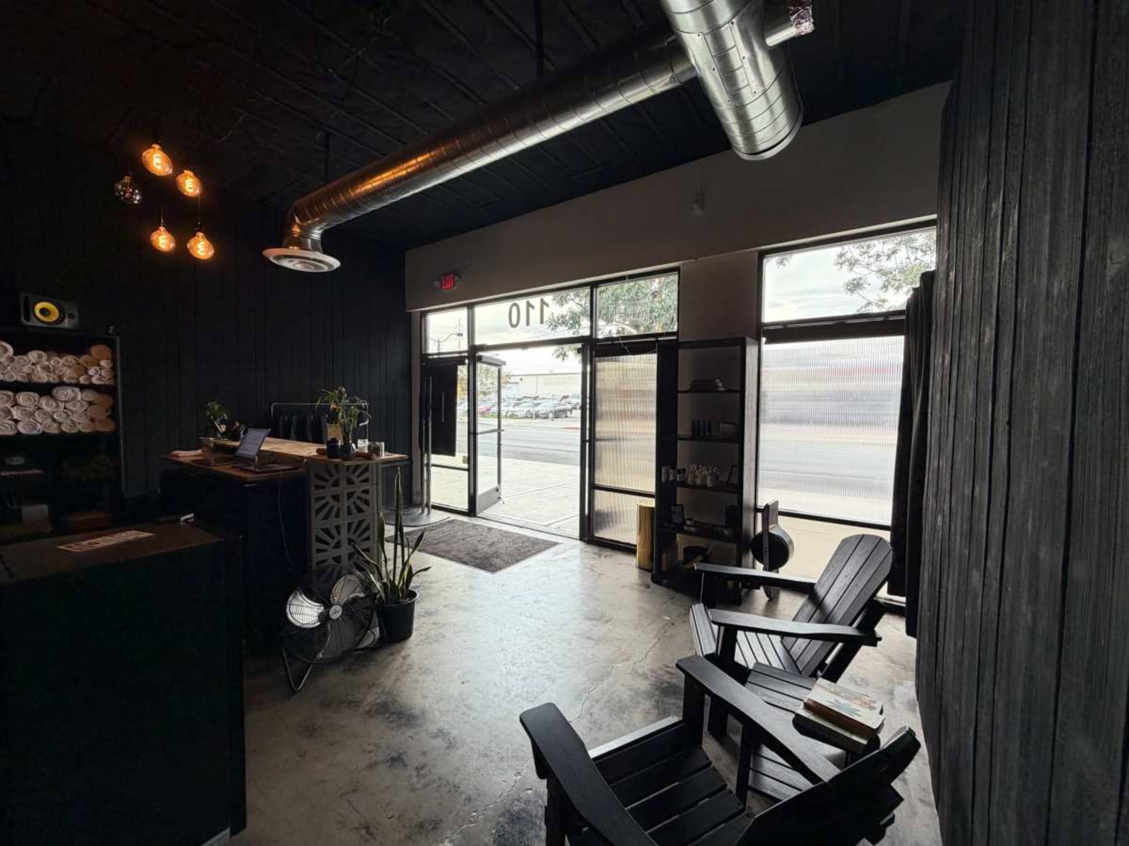 The image shows a minimalist reception area with black walls, two large windows, and black wooden chairs facing the entrance.