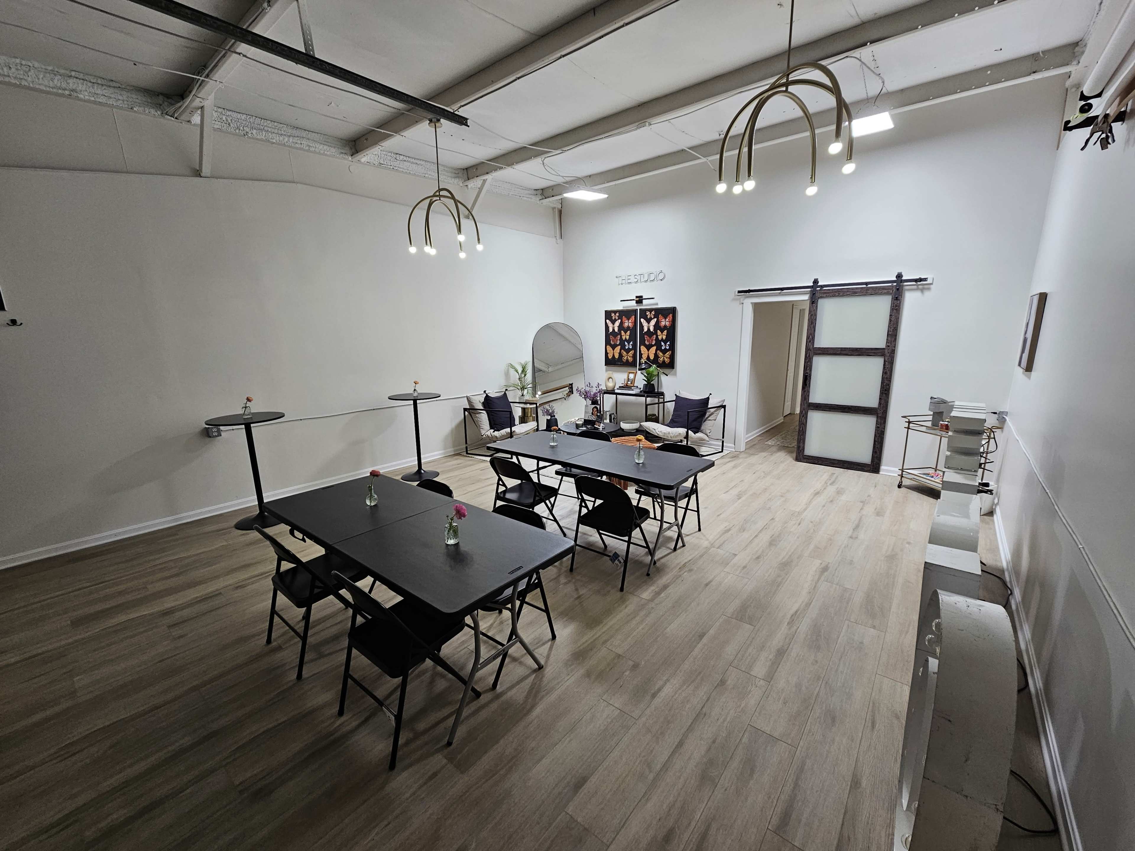 The image shows a spacious, well-lit room with several black tables set for a meeting, surrounded by minimalist decor.