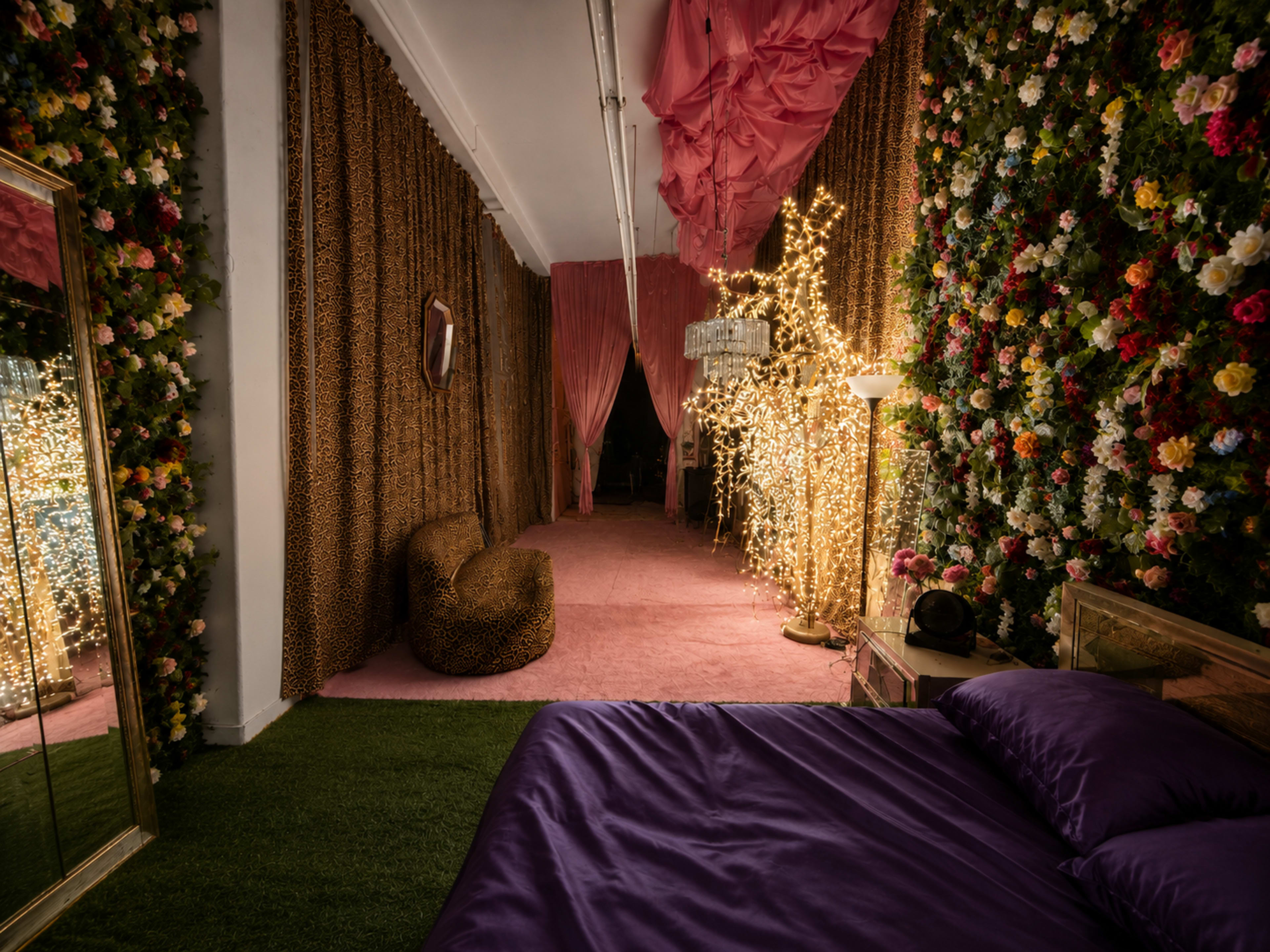 The image shows a decorated interior space resembling a whimsical bedroom with floral walls, soft lighting, and a pink carpet.