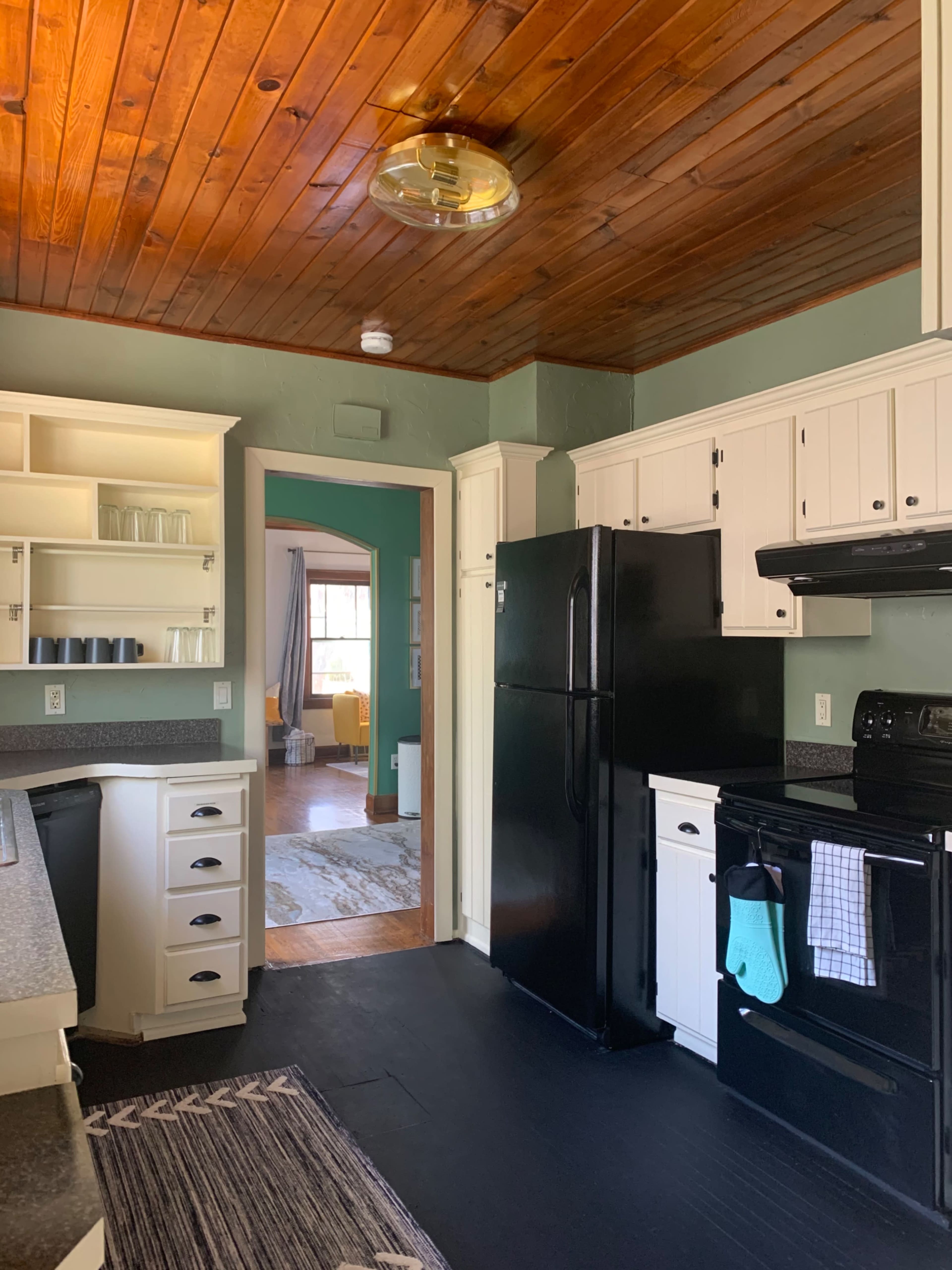 A kitchen with white cabinets, black appliances, and a wood-paneled ceiling.