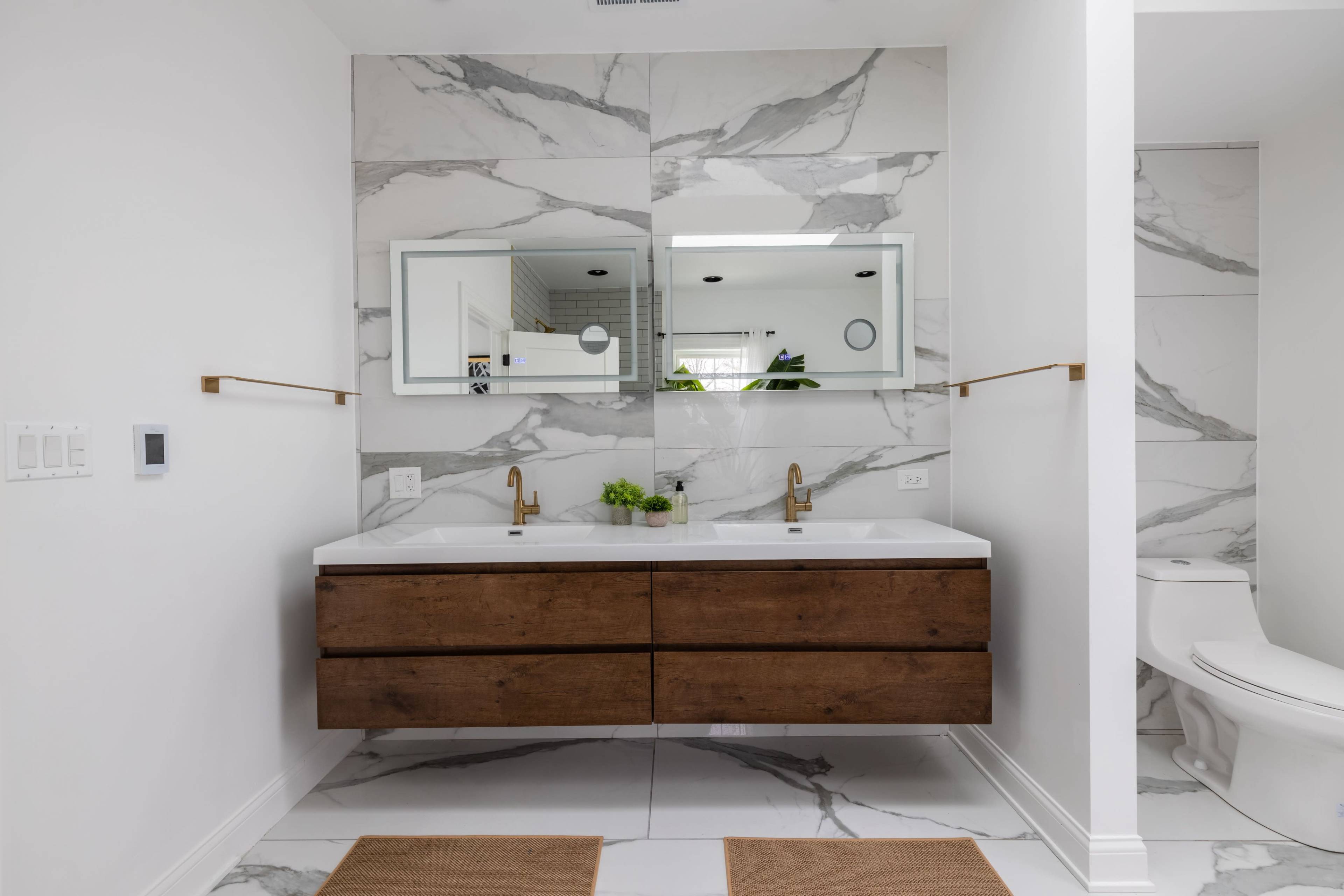 The bathroom features a double vanity with wooden drawers, two mirrors, and a wall of marble tile.