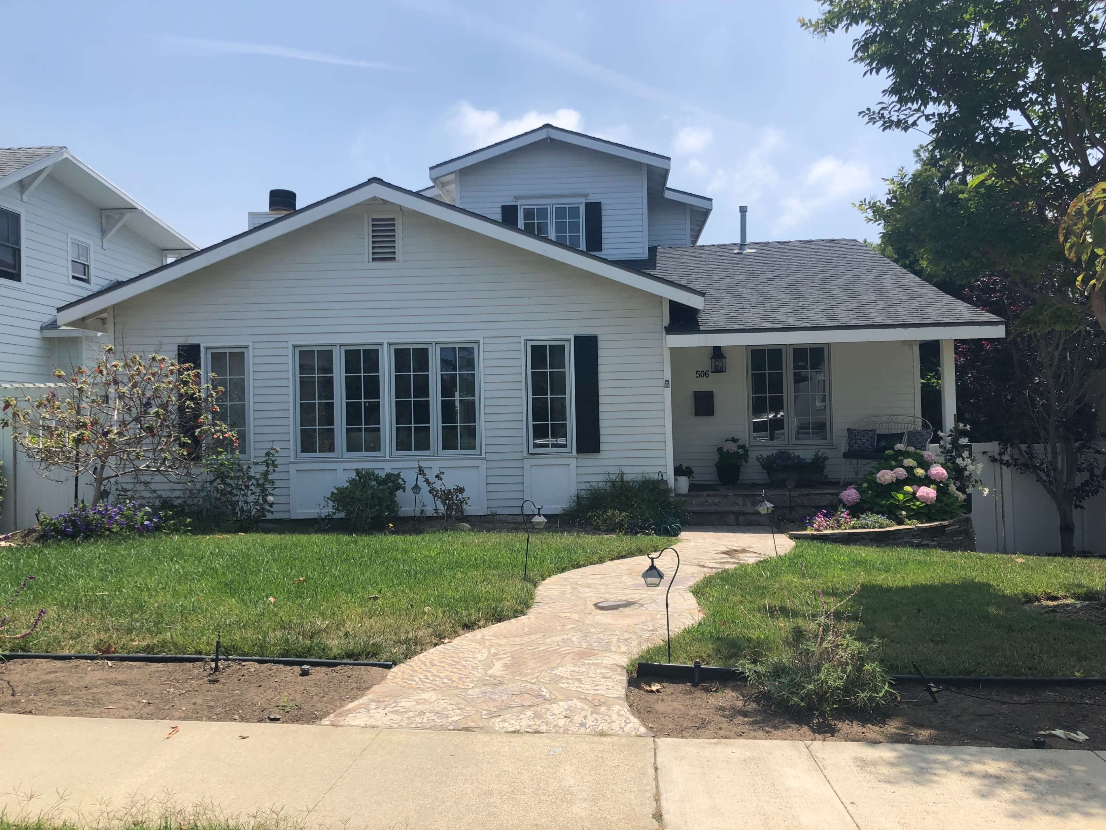 A white wooden house with multiple windows and a neatly landscaped front yard featuring a stone pathway.