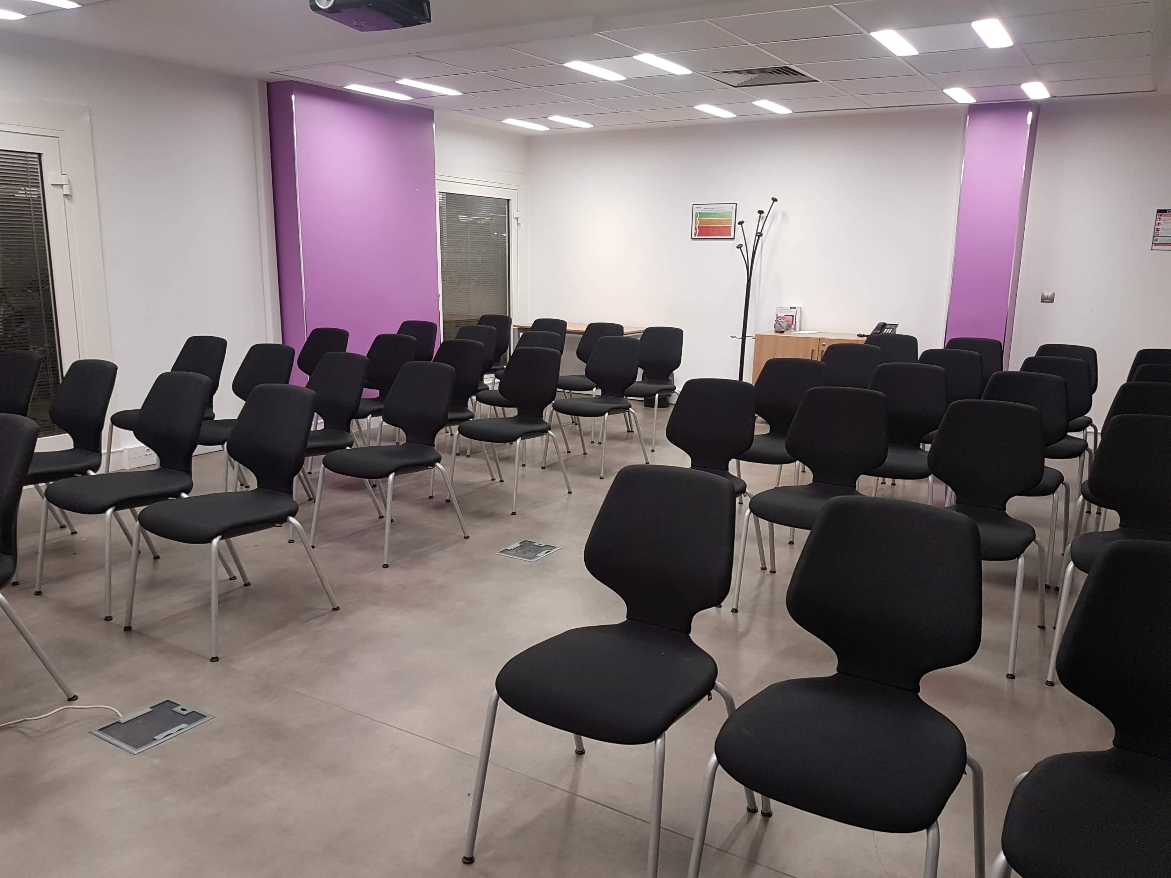 A seminar room with rows of black chairs arranged on a tiled floor, accented by purple walls.