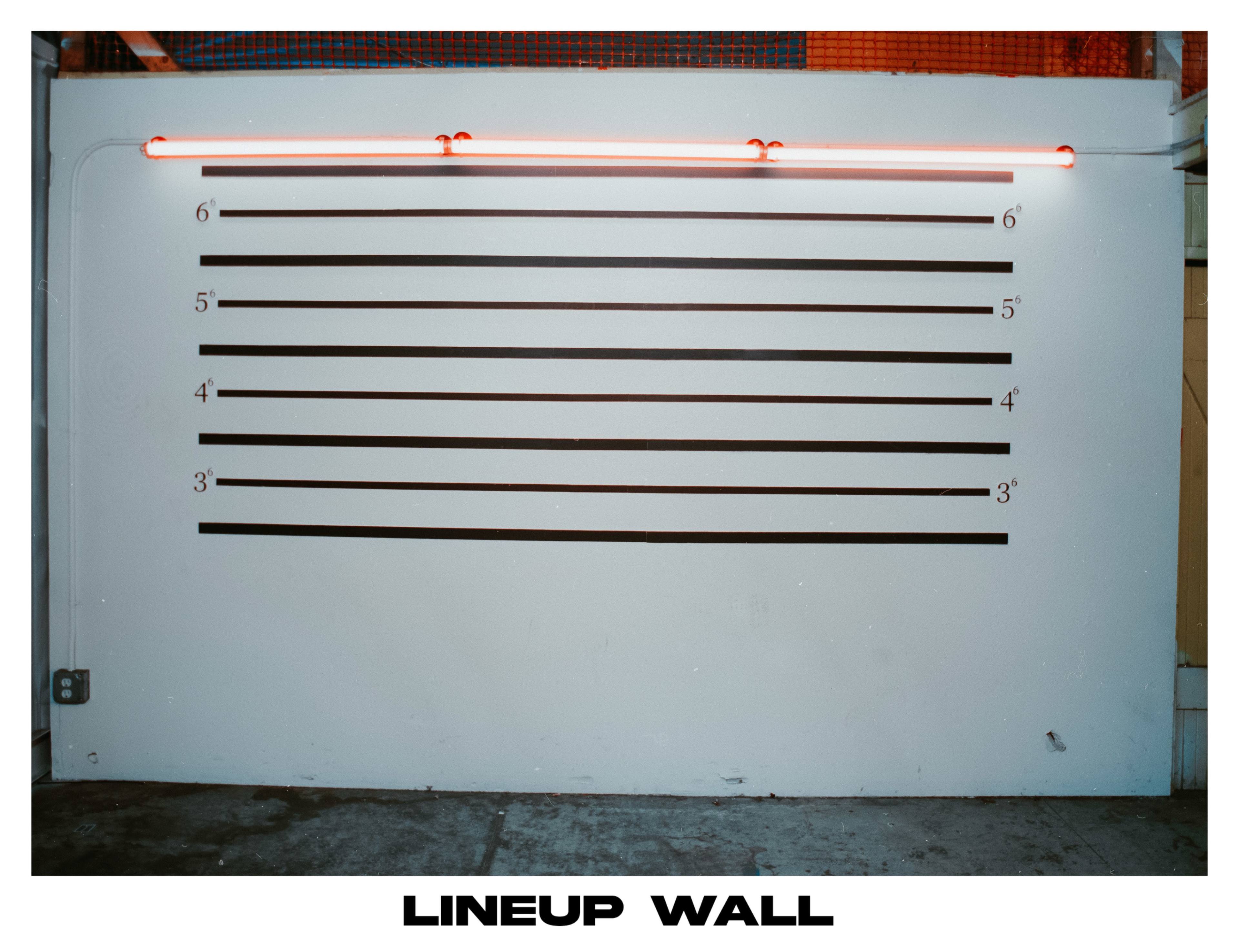 A lineup wall with horizontal measurement lines marked from 3 to 6 feet, illuminated by red neon light.