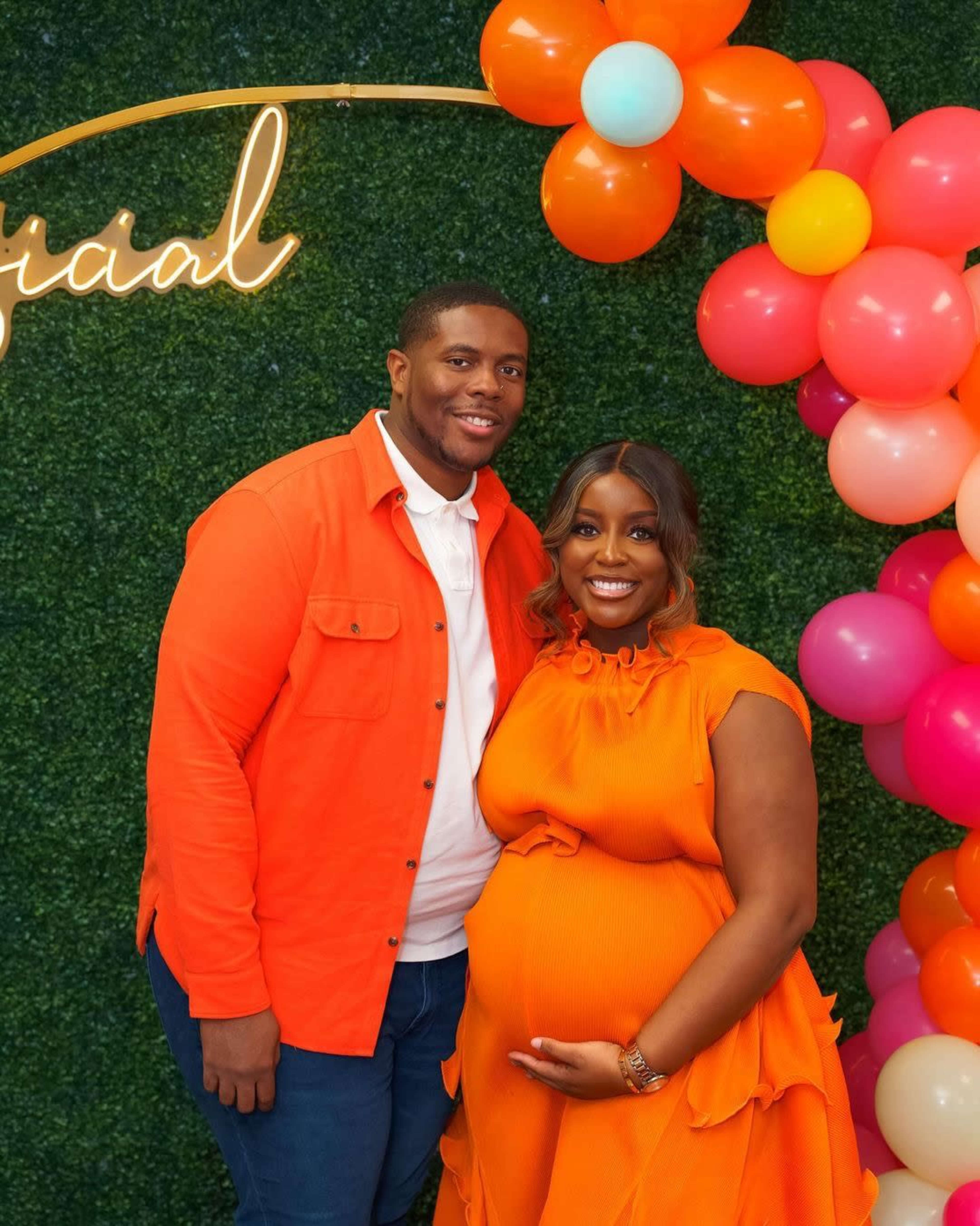 A couple stands together in front of a festive backdrop adorned with balloons, celebrating a special occasion.