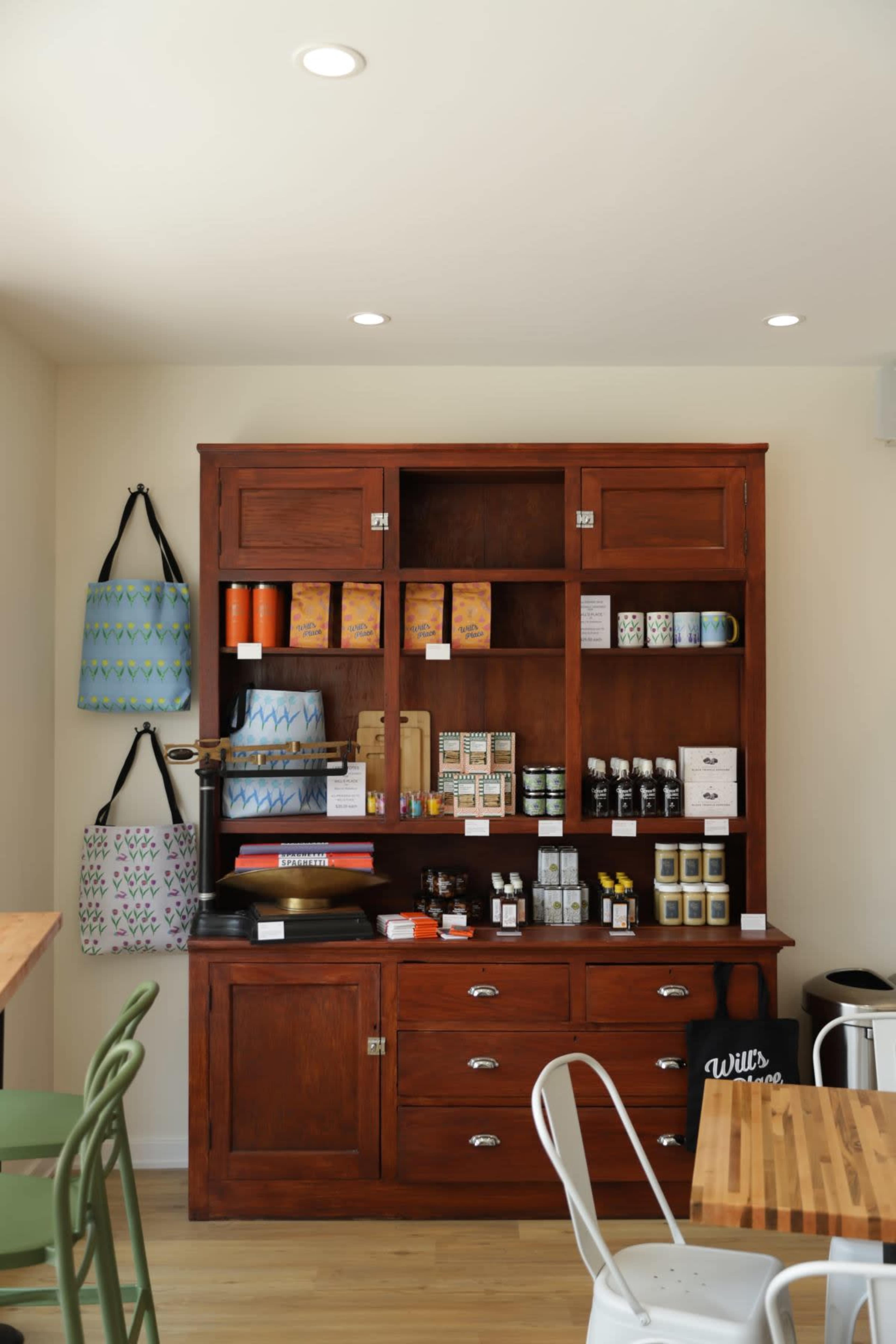 A wooden display cabinet filled with various packaged goods and condiments is positioned against a light-colored wall in a café setting.