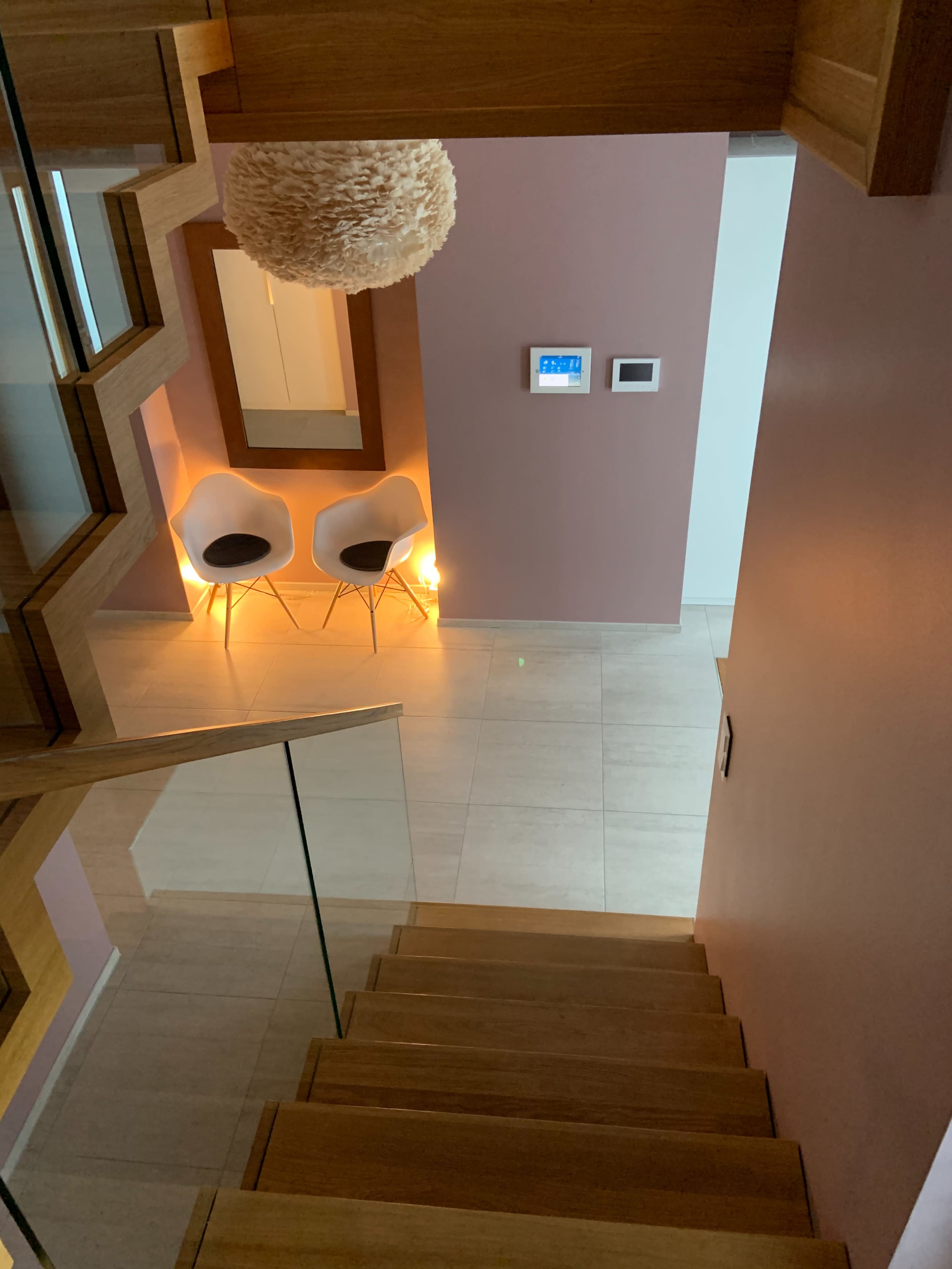 A staircase leads down to a foyer with two chairs beside a decorative mirror and a wall-mounted control panel.