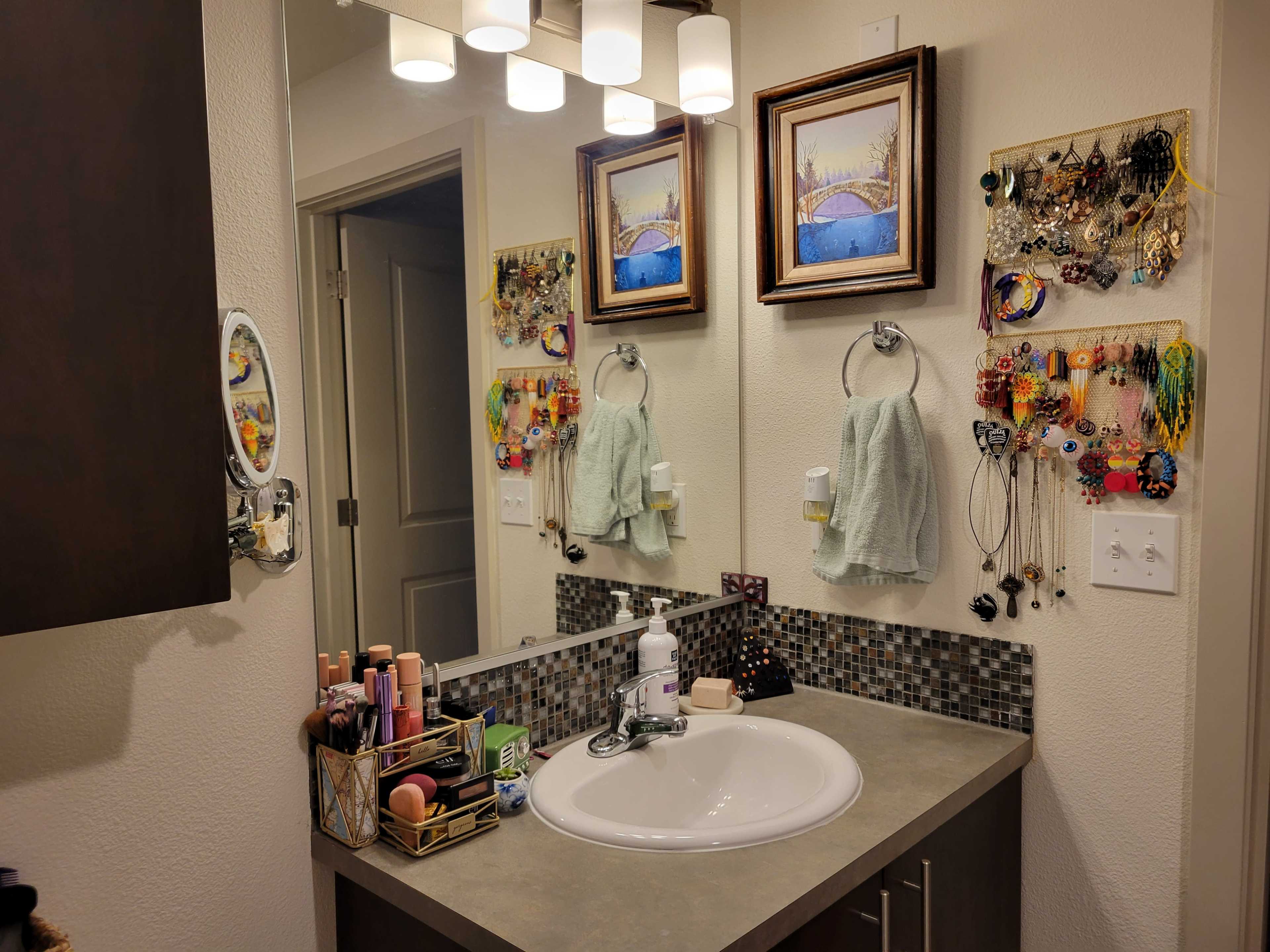 A bathroom with a dual sink vanity, wall-mounted art, and organized jewelry displays.