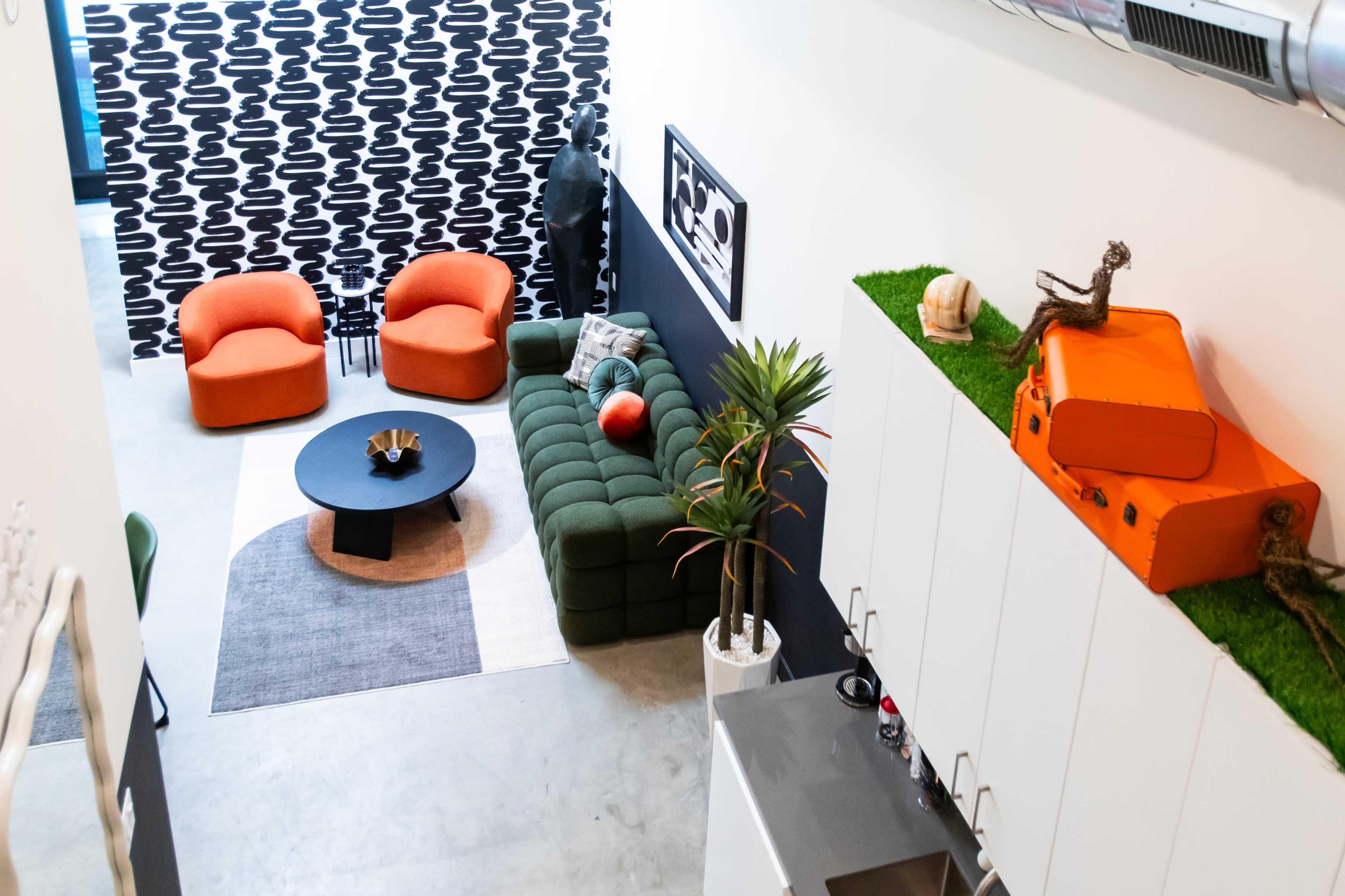 A modern living space with orange armchairs, a green sofa, a round black table, and a combination of decorative plants and sculptures.