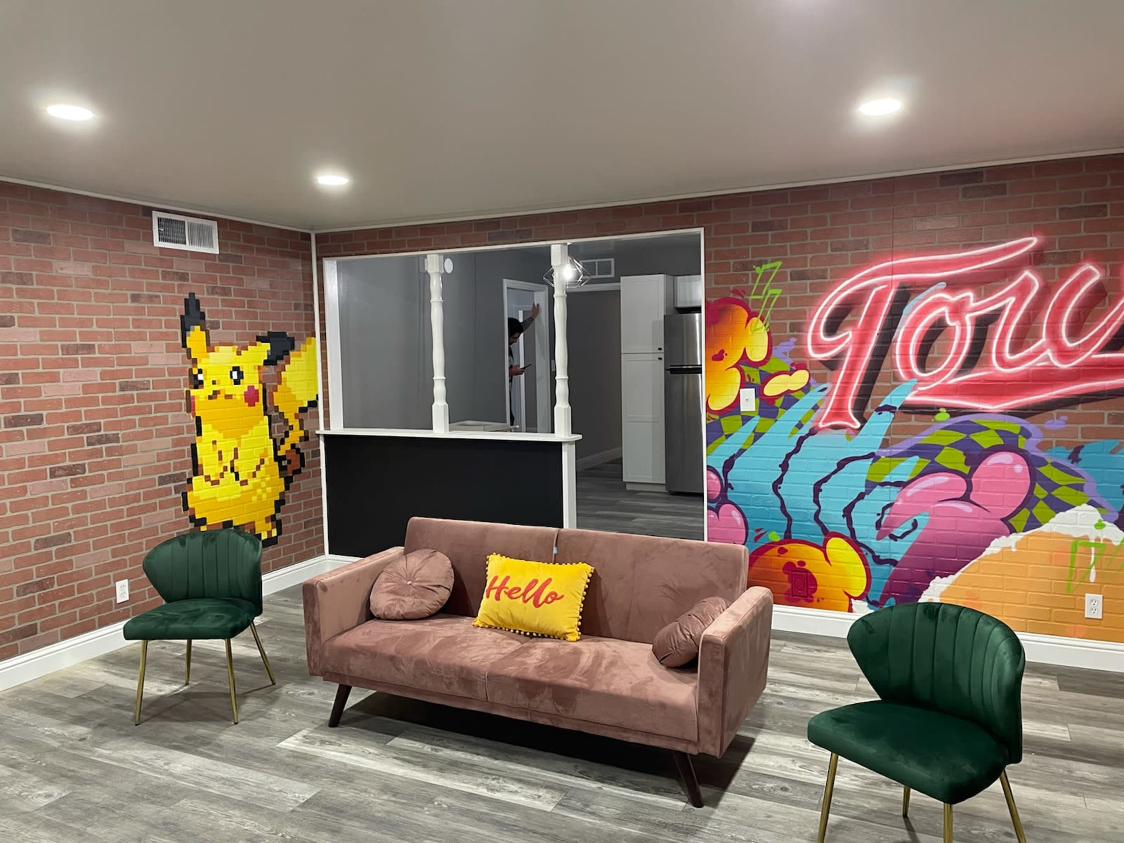 A modern living space with a pink sofa, green chairs, and vibrant wall murals featuring a Pikachu and colorful graffiti.