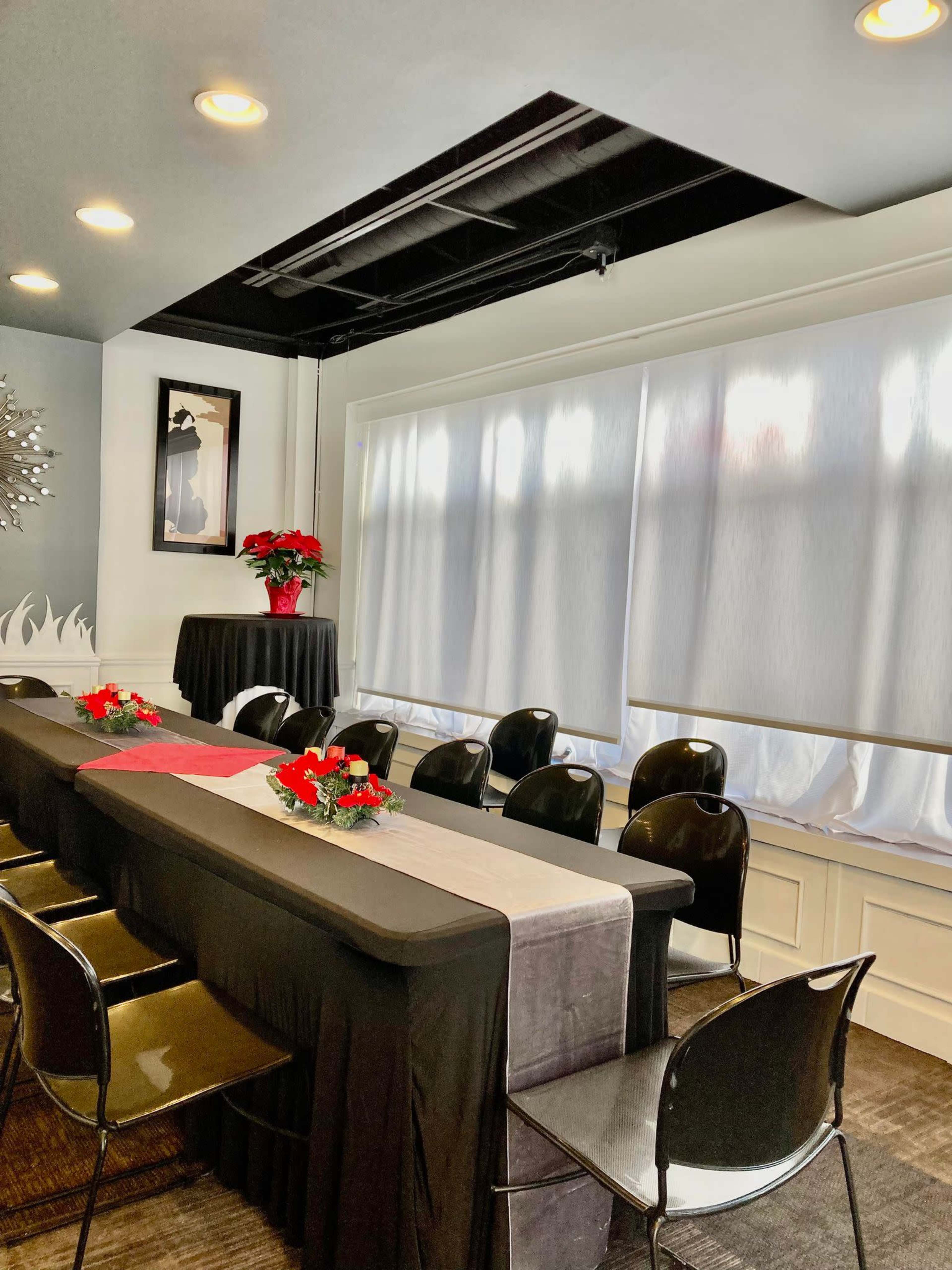 A decorated meeting room features a long table with a black tablecloth, surrounded by black chairs, and adorned with red floral centerpieces.