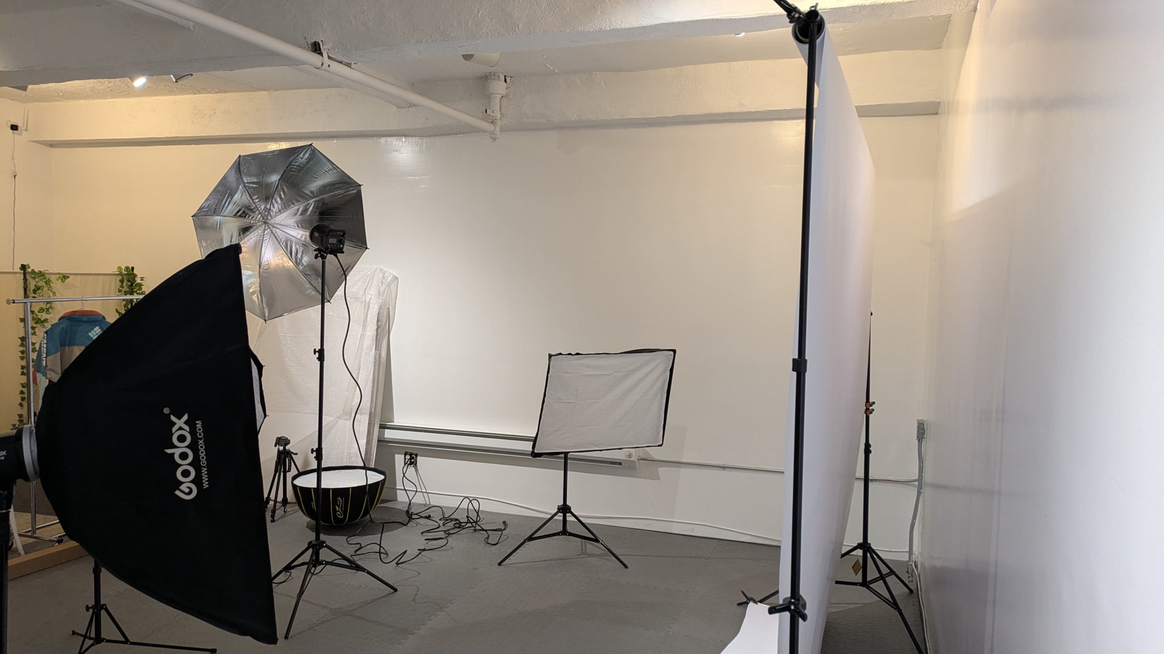 The image shows a photography studio with lighting equipment, backdrops, and a setup for shooting.