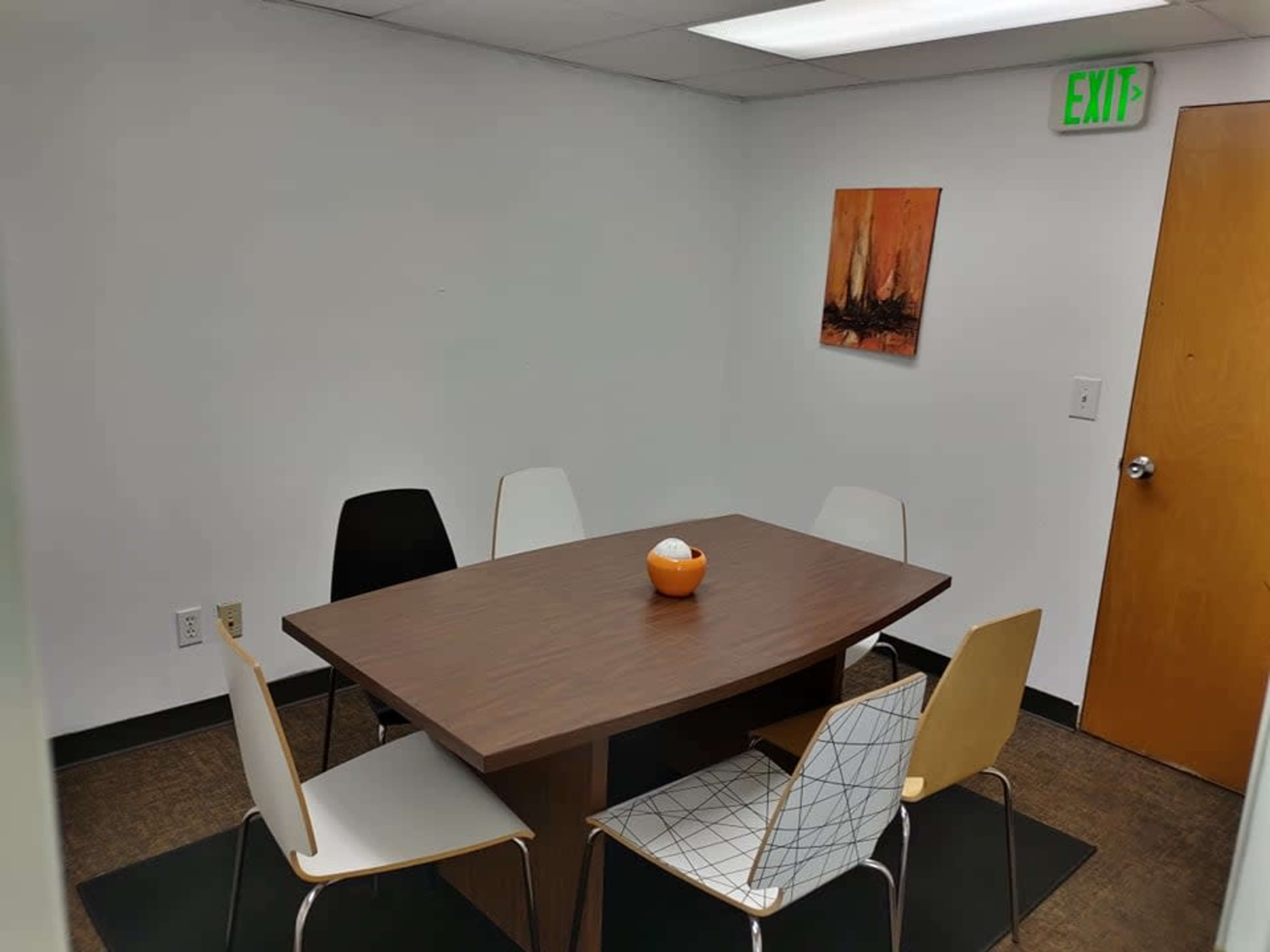 A small meeting room features a wooden table surrounded by four chairs and a wall-mounted artwork.