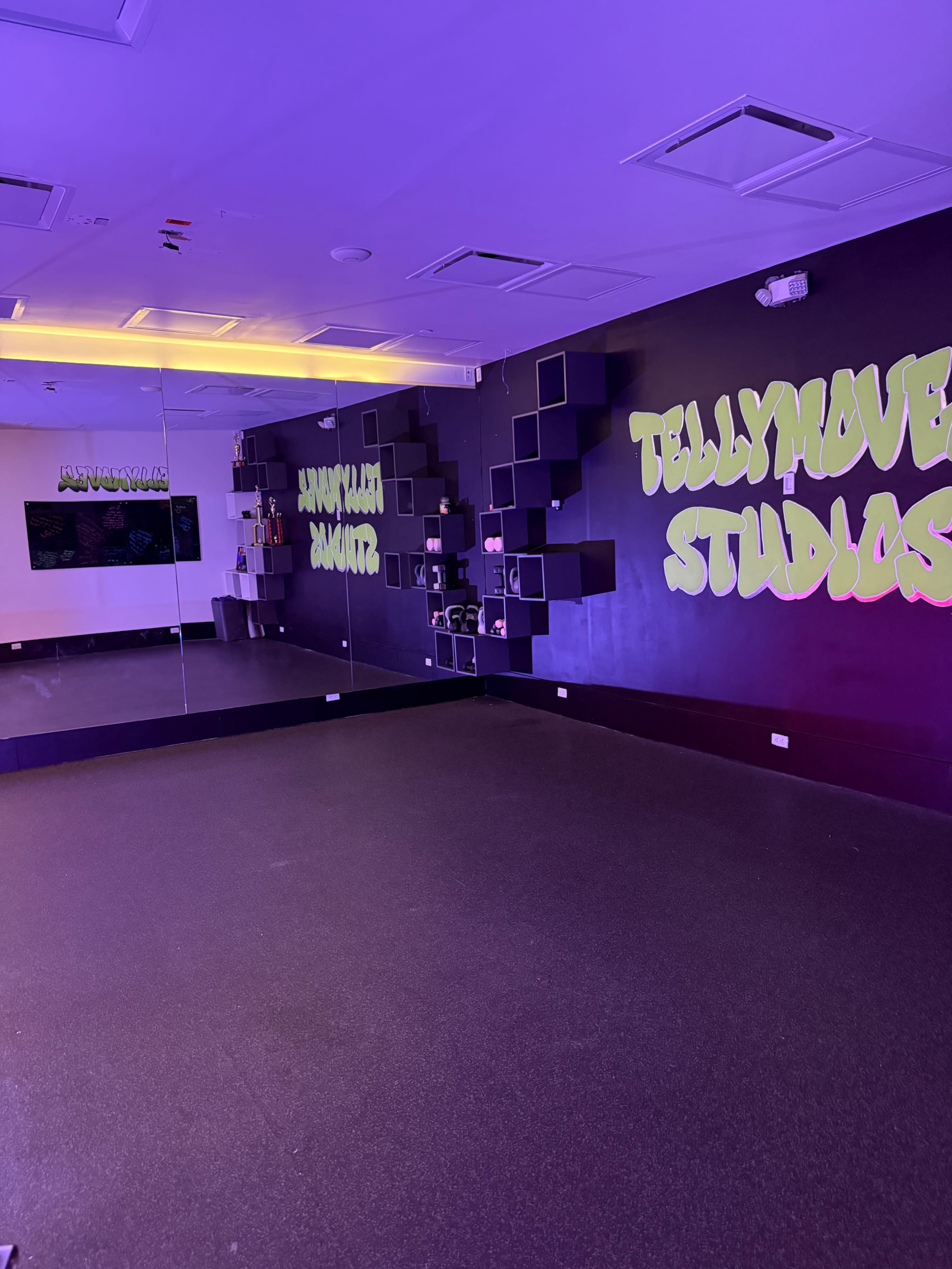 The image shows a brightly lit dance studio featuring a large mirror and colorful wall decorations that read "Tellymove Studios."