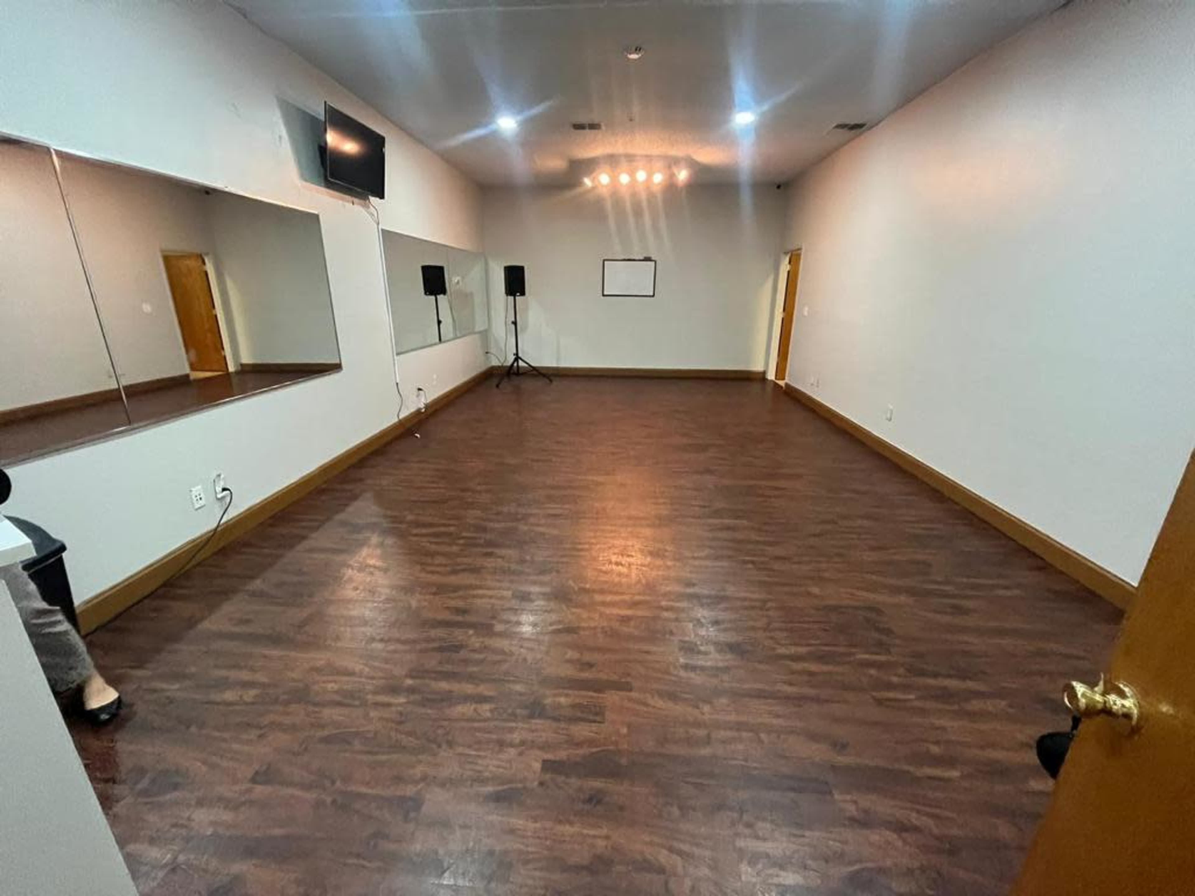 A spacious, empty room with wooden floors, a large mirror on one wall, and a television mounted on another wall.