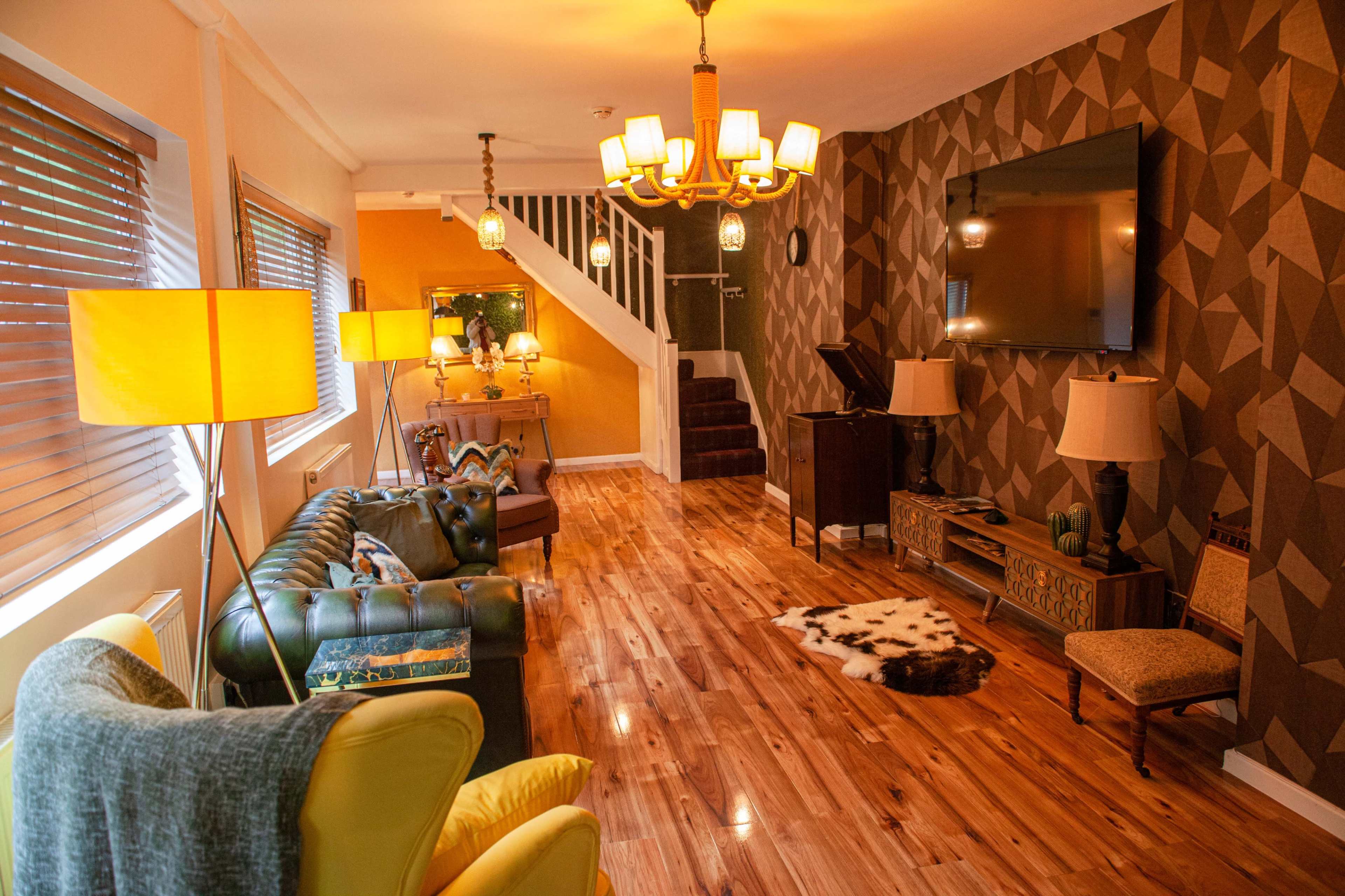 A spacious living room featuring a mix of leather and fabric seating, wooden flooring, and decorative wall patterns.